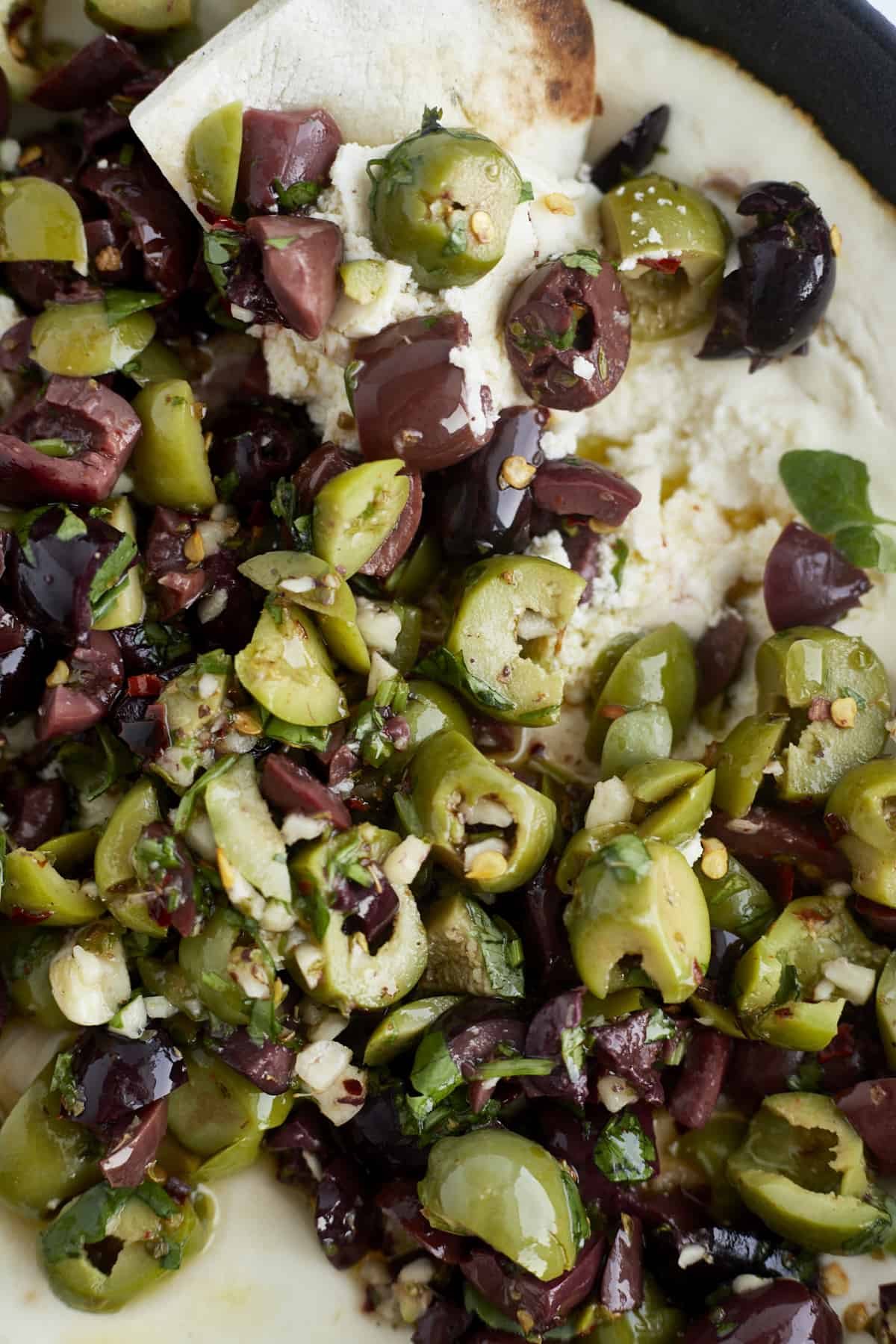 close up image of a piece of bread being dipped into warm feta topped with marinated olives