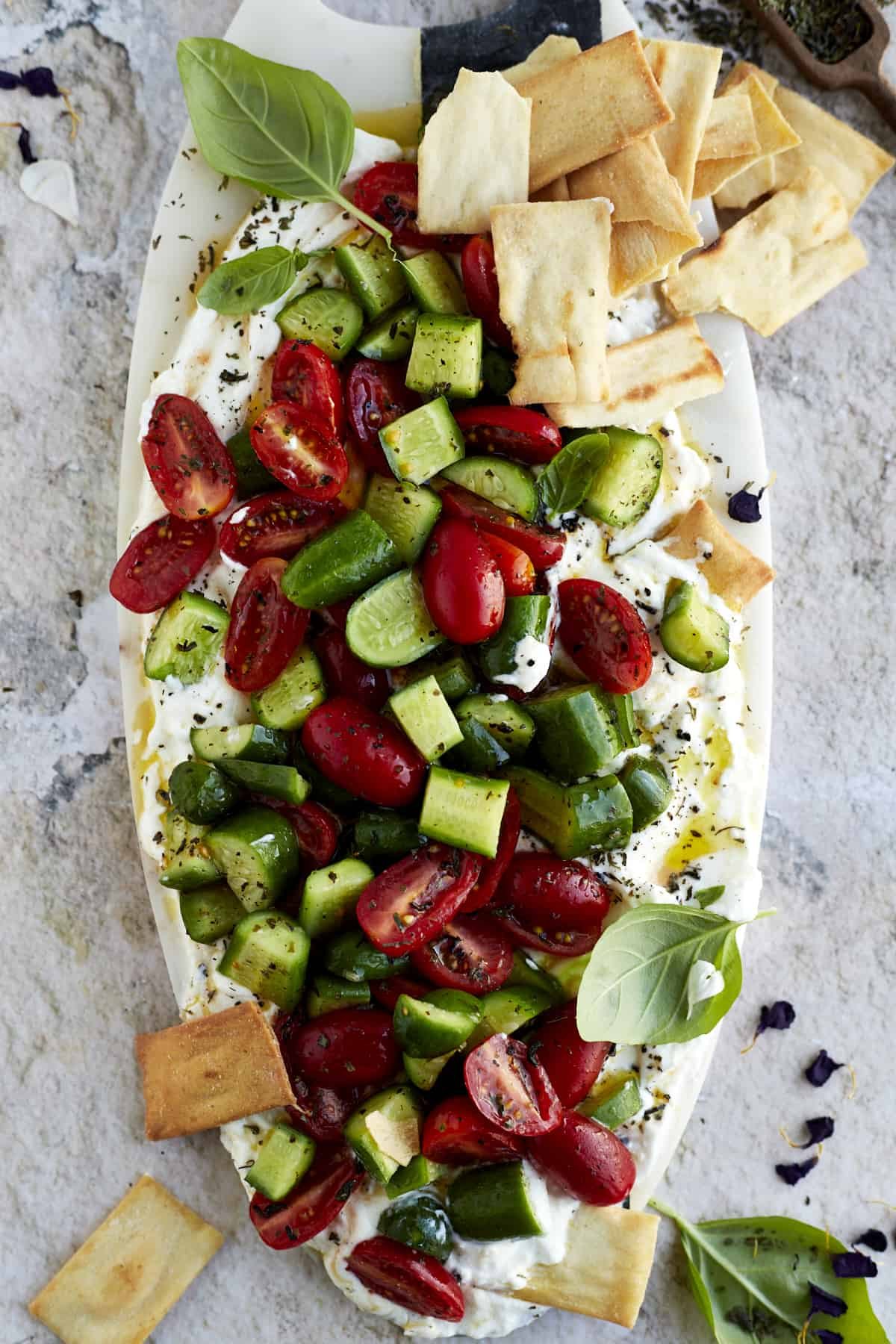 overhead image of cucumber and tomato salad layered over whipped feta dip with pita chips on the side