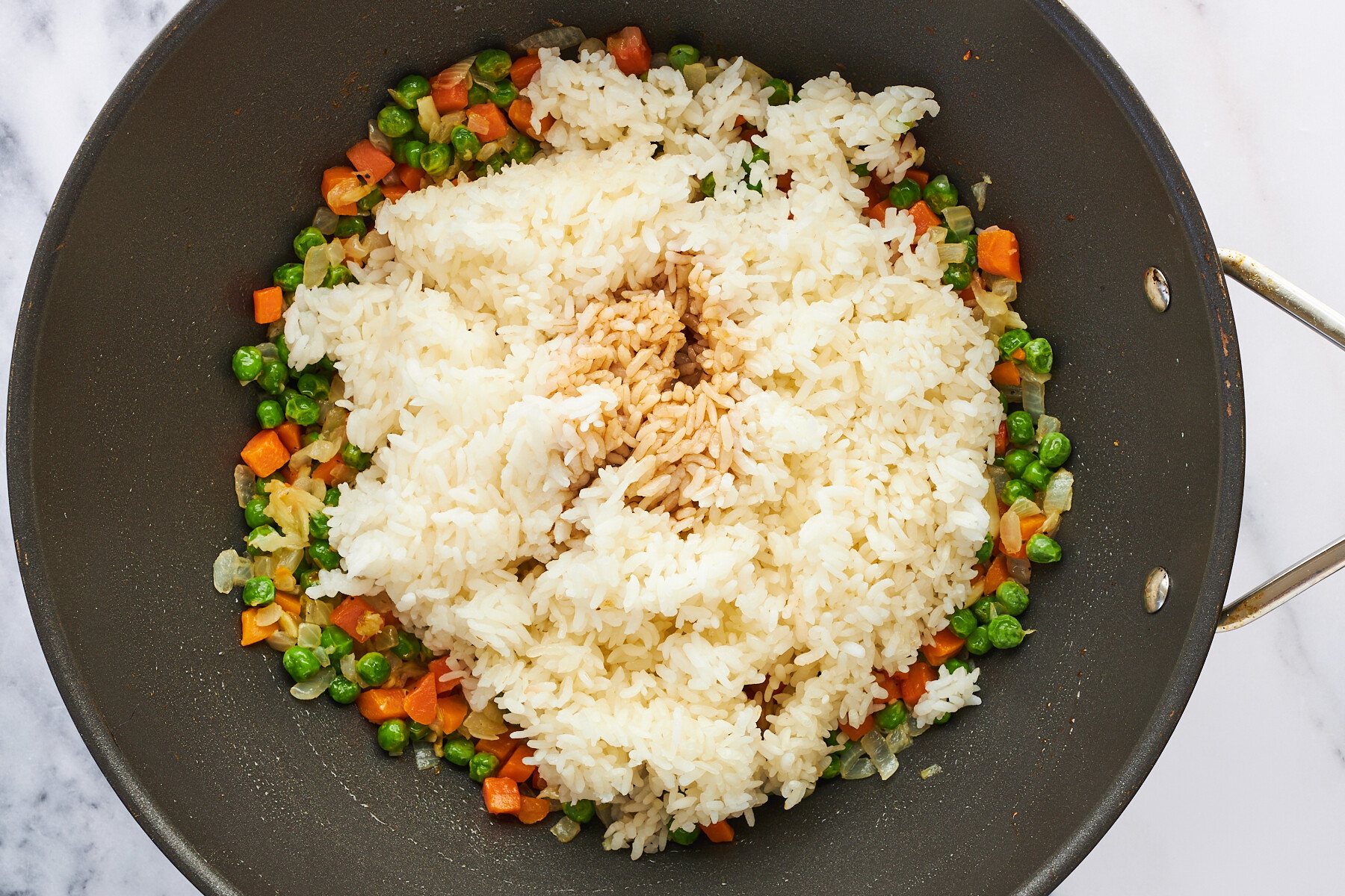 Rice and soy sauce being added to veggies in a wok.