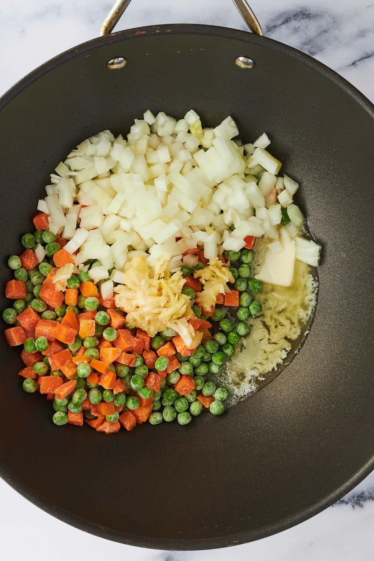 Peas and carrots, onion, butter, and garlic in a wok.