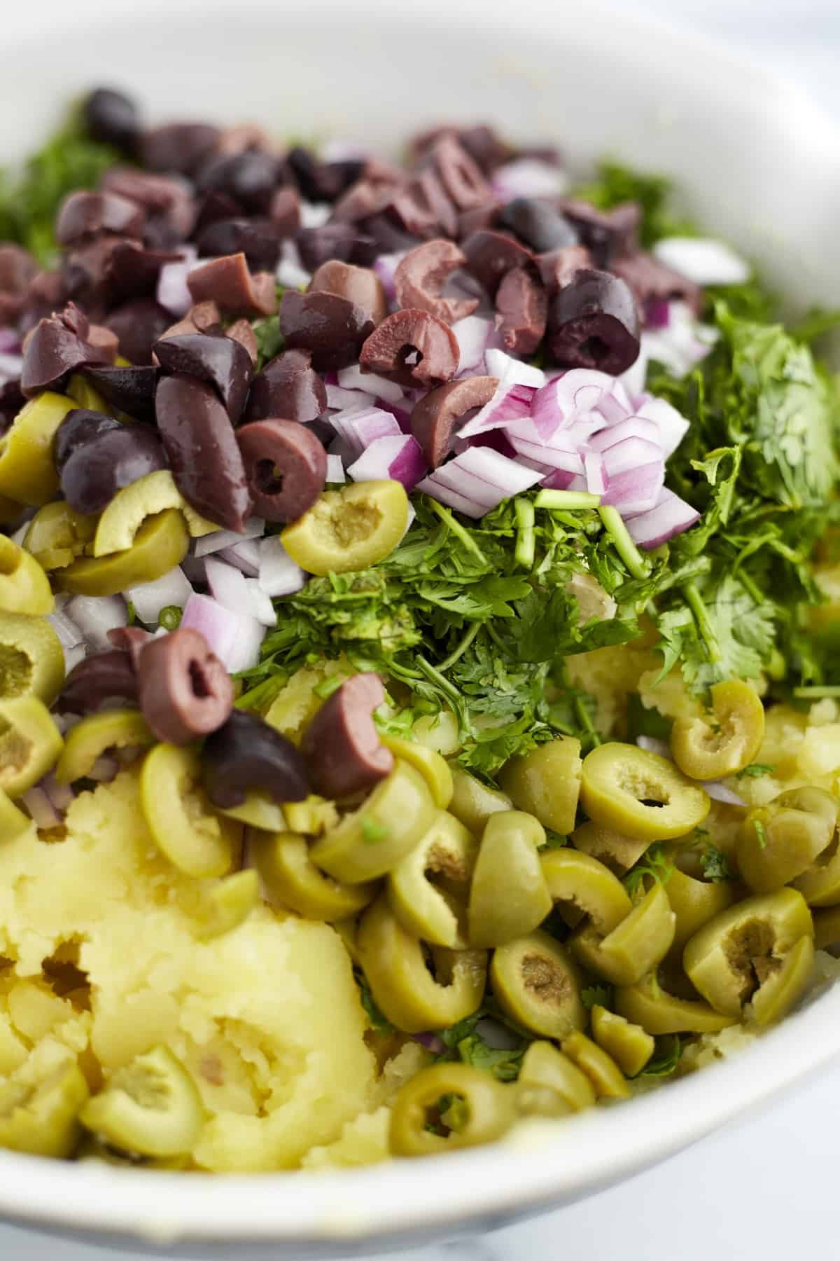 overhead image of yukon gold mashed potatoes topped with garlic, olives, and herbs ready to be stirred.