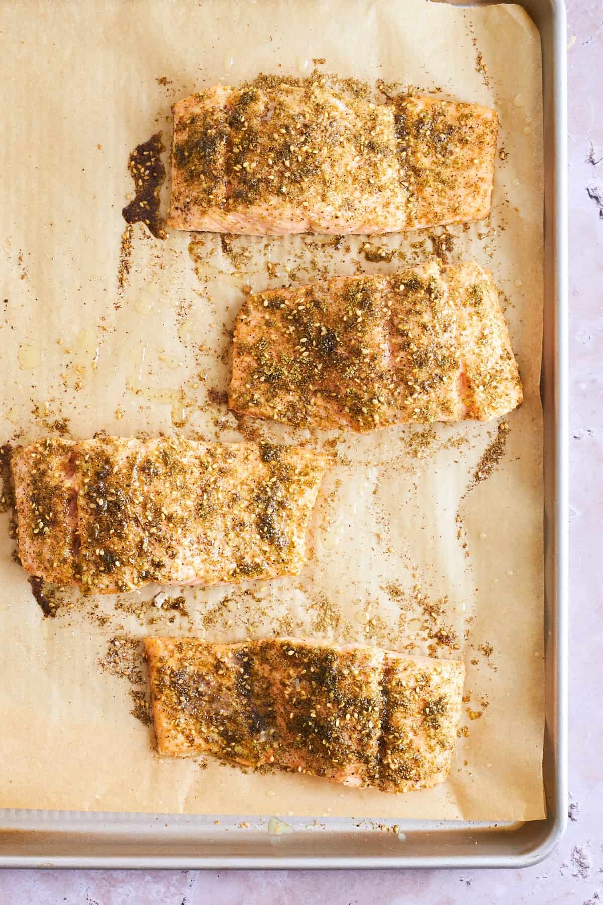 Za'atar seasoned baked salmon on a parchment paper-lined baking sheet.