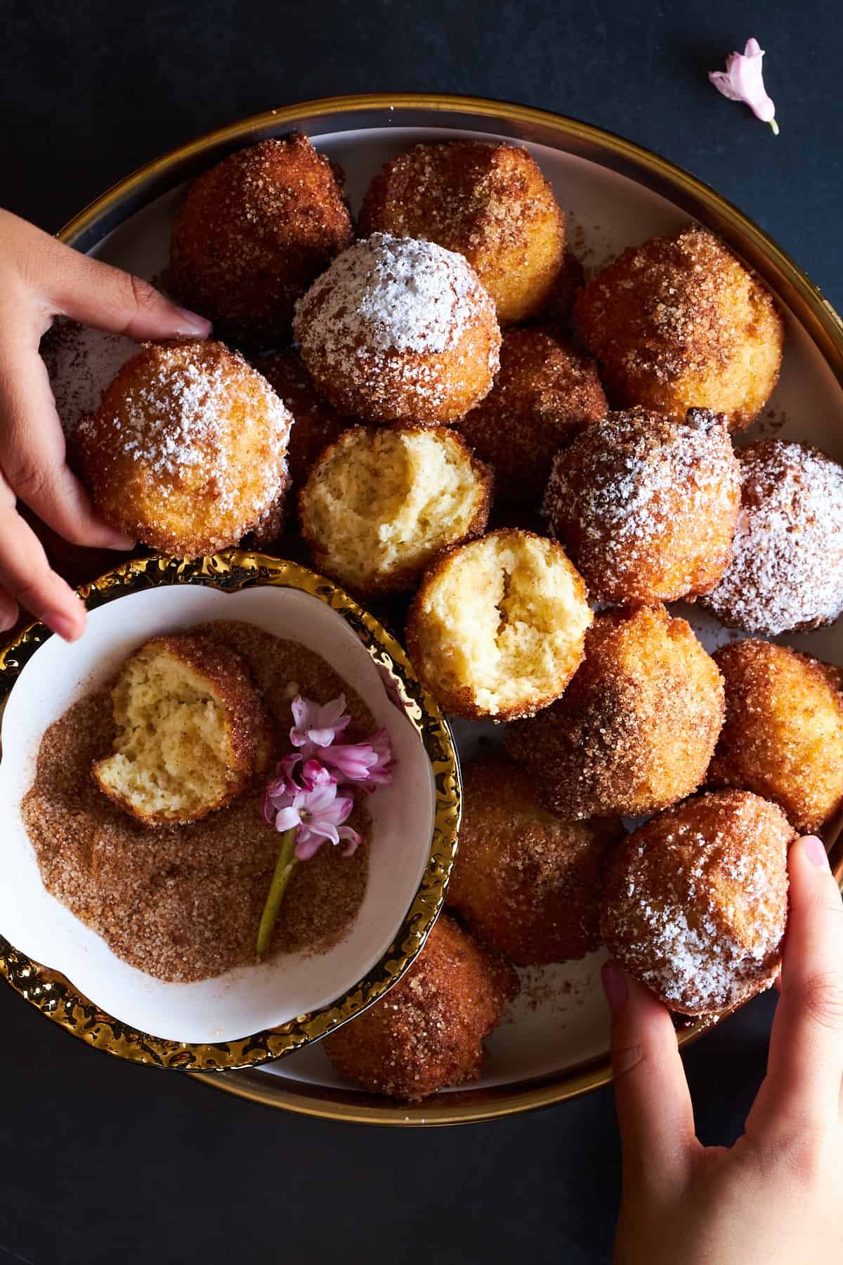 Hands grabbing zeppole donuts from a plate.