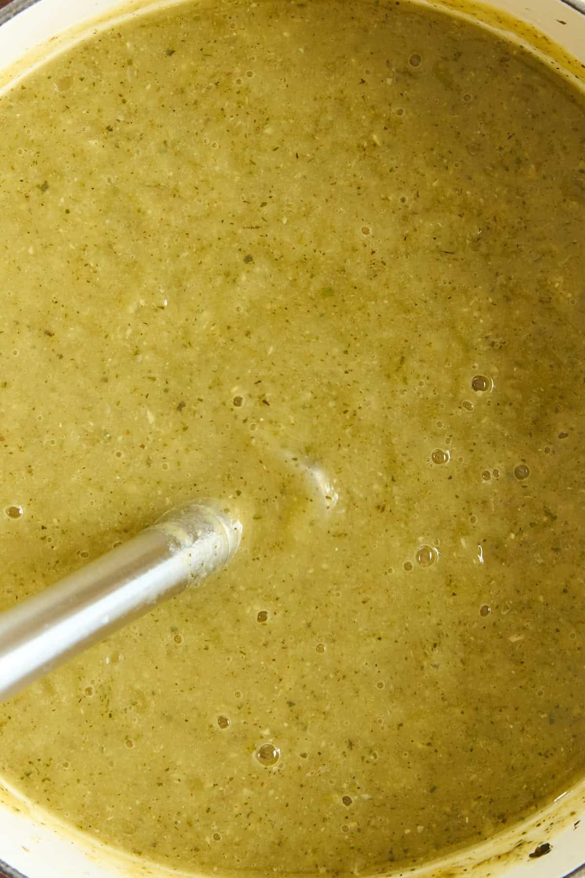 An immersion blender blending a pot of green vegetable soup, creating a smooth and creamy texture.