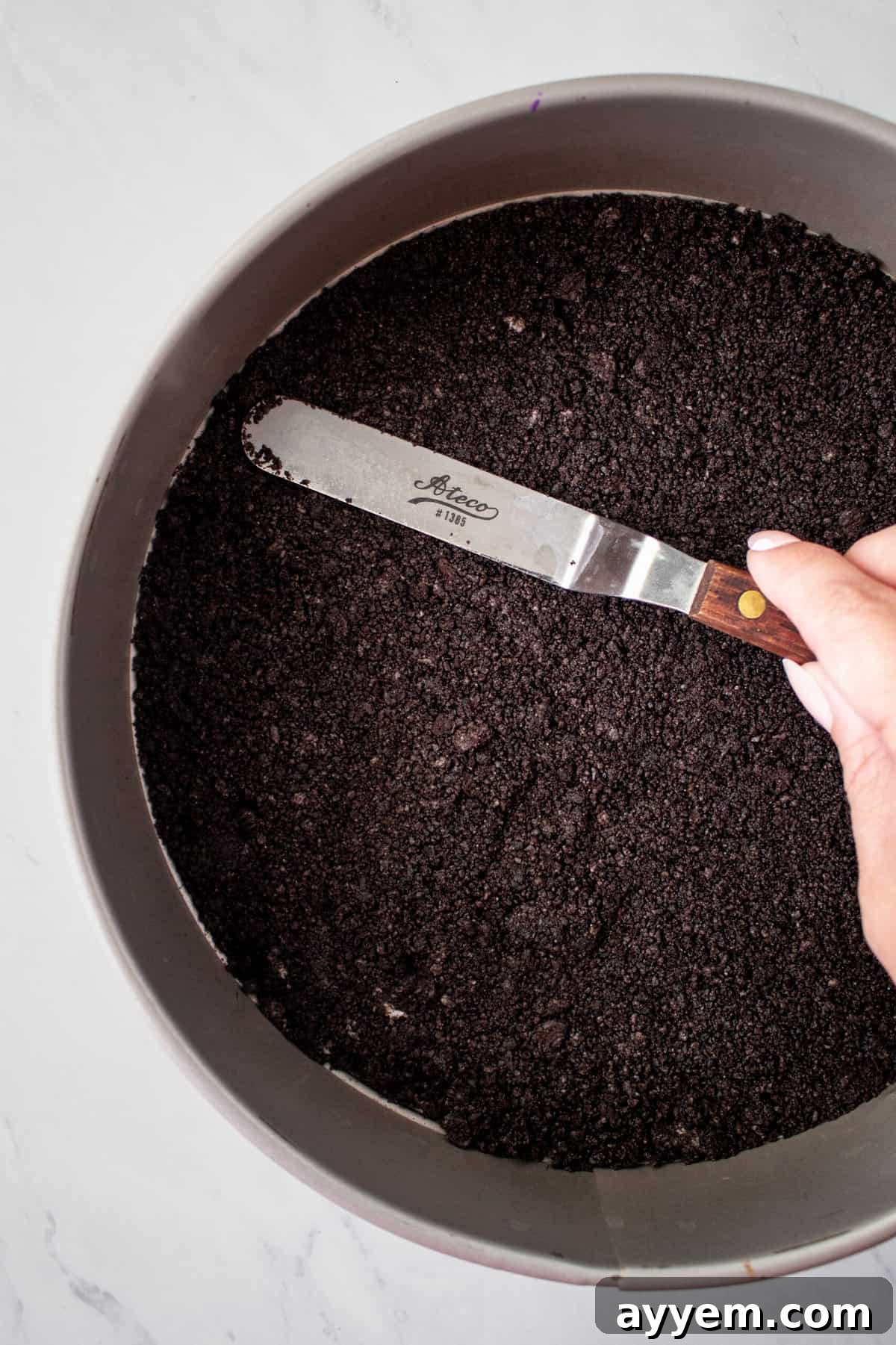 Smooth Oreo cookie crust being pressed into the bottom of a pie tin, forming the perfect base for a Billy Miner Ice Cream Pie.