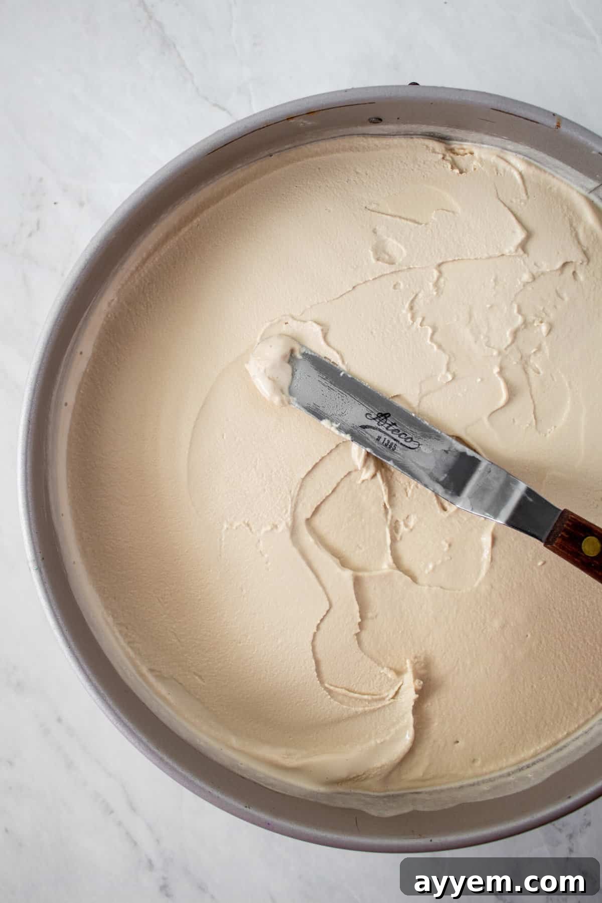 Smooth coffee ice cream being spread evenly over a chocolate cookie crust, forming a delicious layer for the ice cream pie.