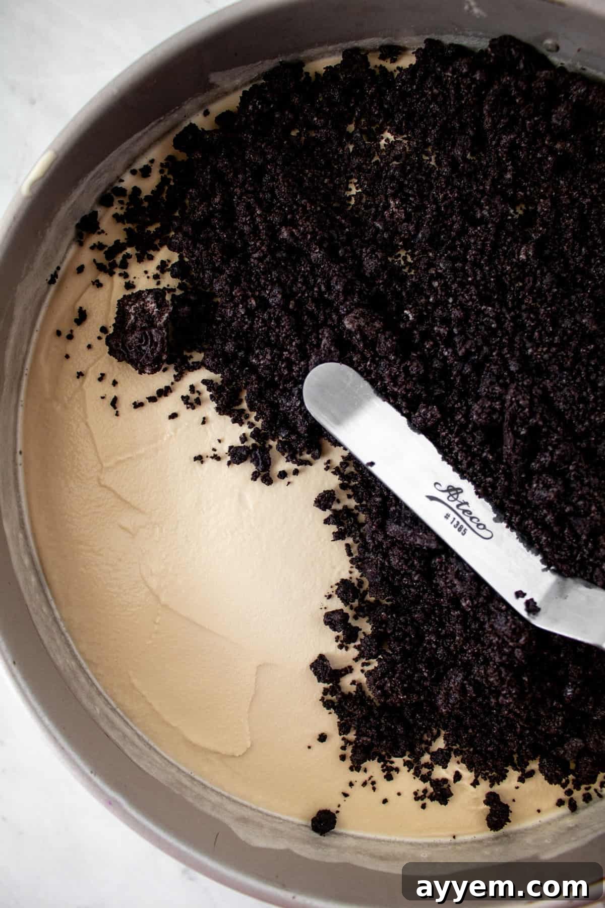 An additional layer of chocolate cookie crust being carefully smoothed over coffee ice cream, creating a delightful double-crust effect.