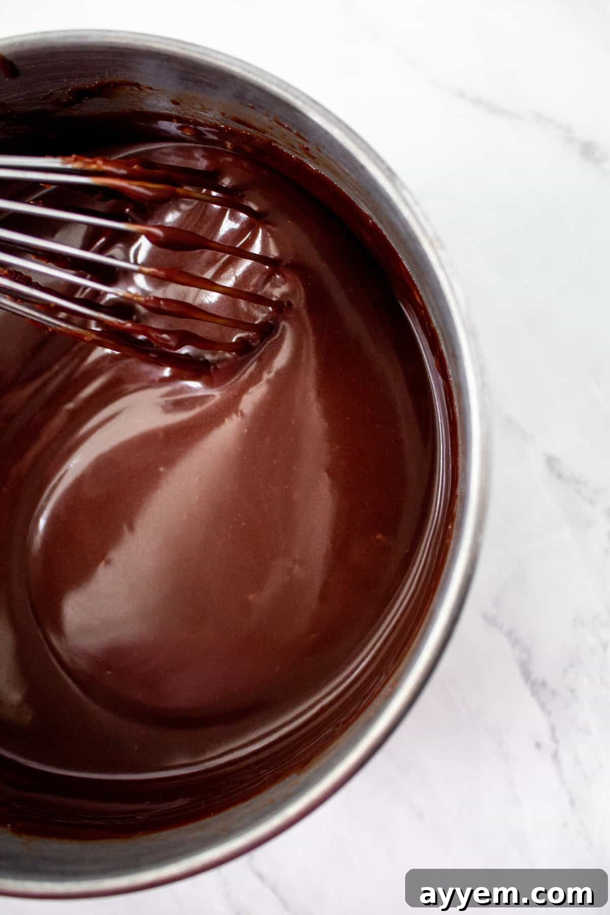 Rich chocolate fudge topping being whisked to a smooth consistency, perfect for the decadent layers of the ice cream pie.
