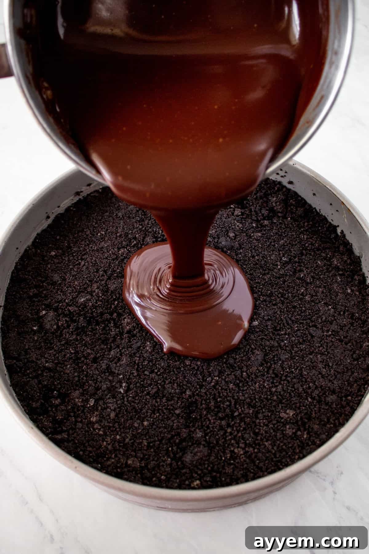 Silky chocolate fudge being poured generously over a layer of chocolate cookie crust and coffee ice cream, creating an irresistible layer.