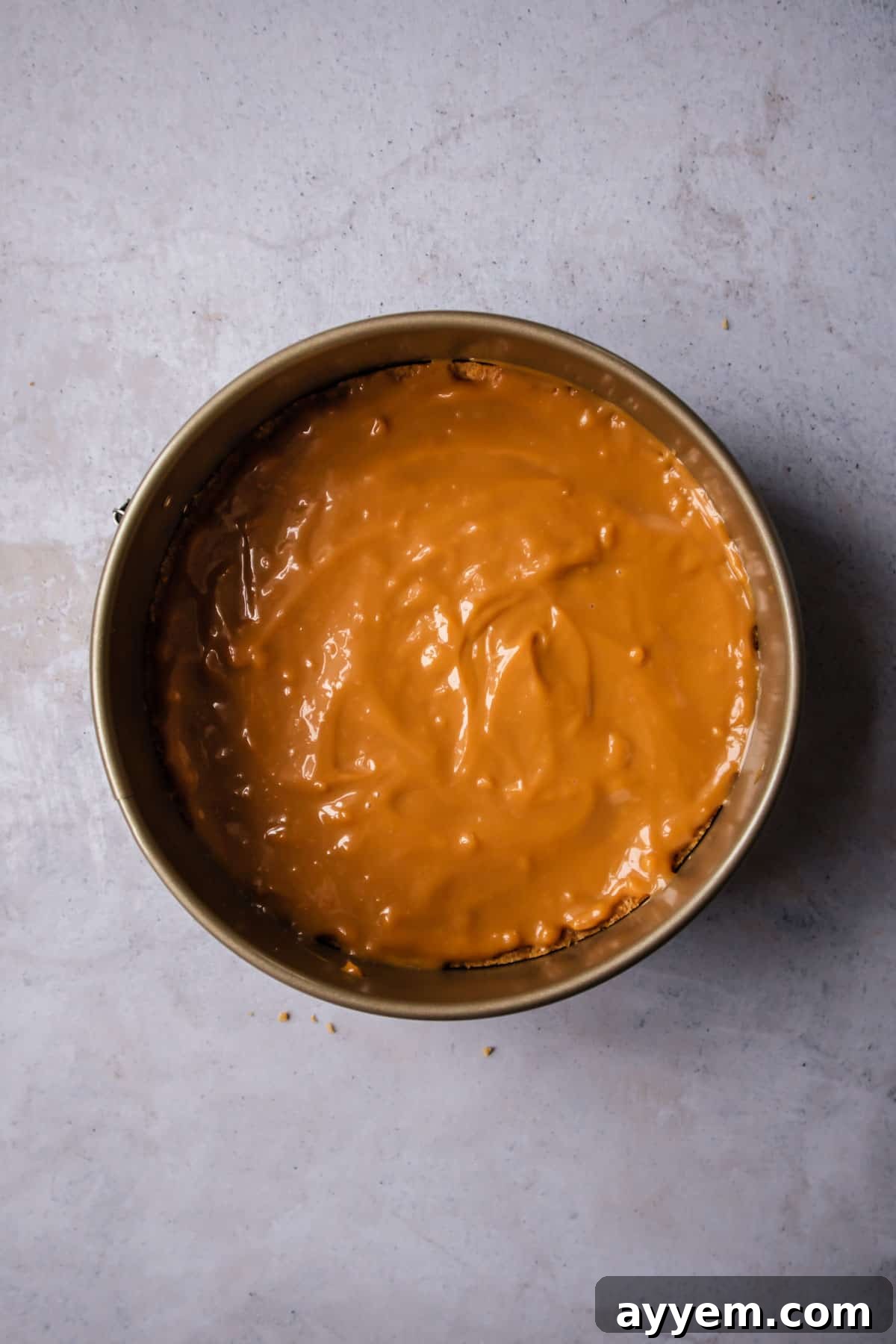 A thick, glossy layer of homemade dulce de leche spread evenly over a golden graham cracker crust in a pie pan, ready for the next delicious layer.