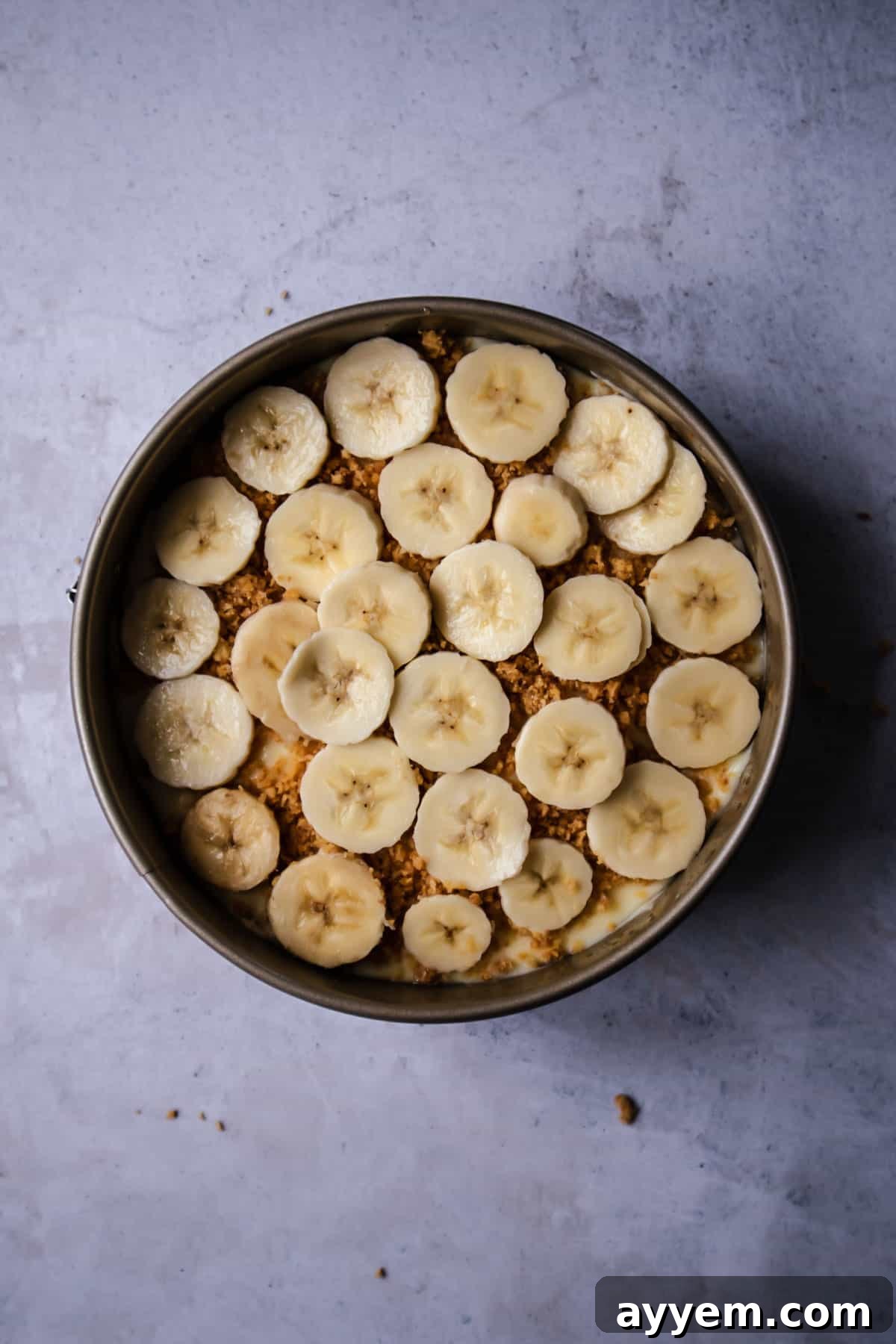 A second, carefully arranged layer of fresh banana slices placed over the graham cracker crumbs on the banoffee pie, ensuring banana in every bite.