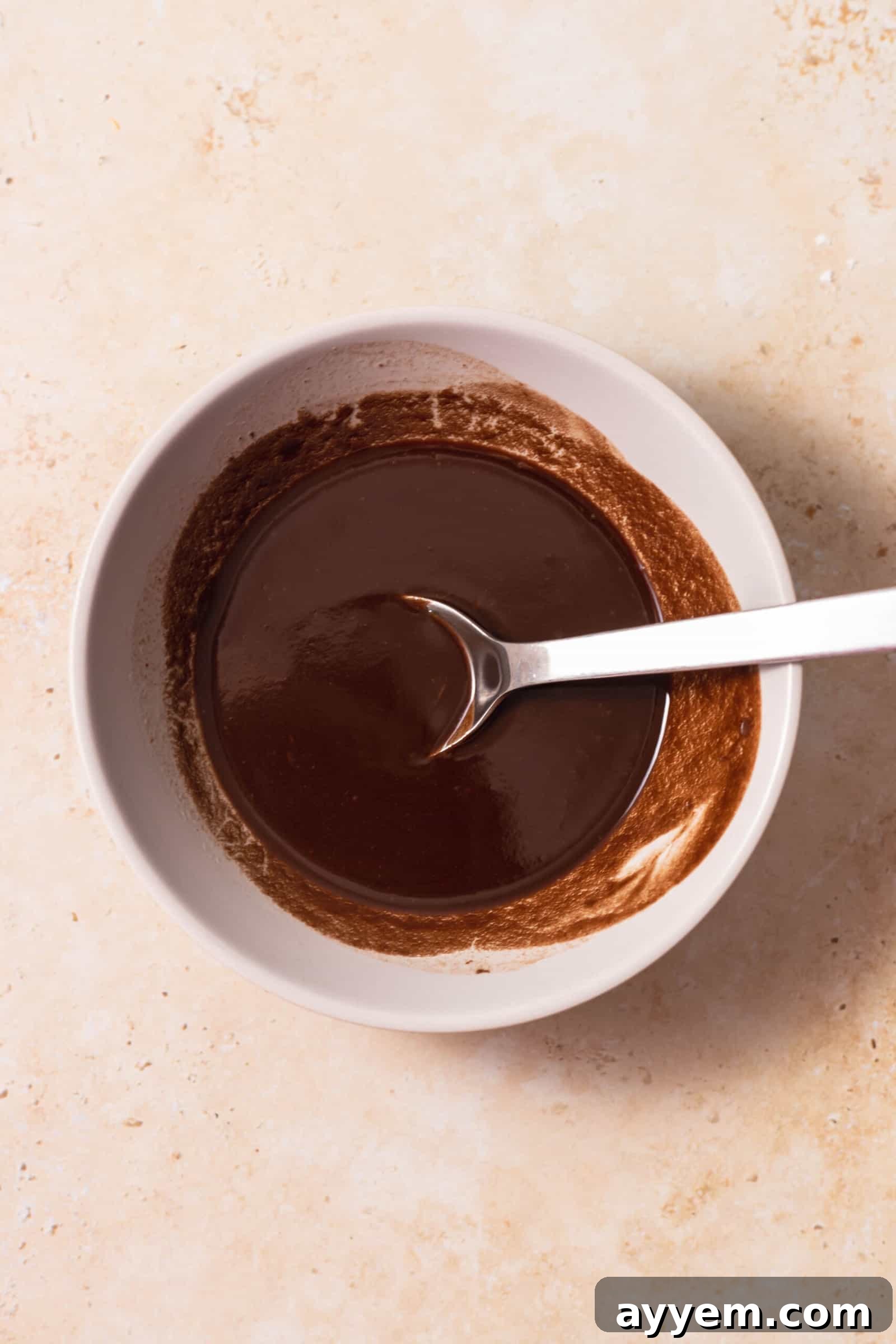 Smooth, melted chocolate and butter mixture in a bowl with a spoon, demonstrating the perfect consistency before adding dry ingredients.