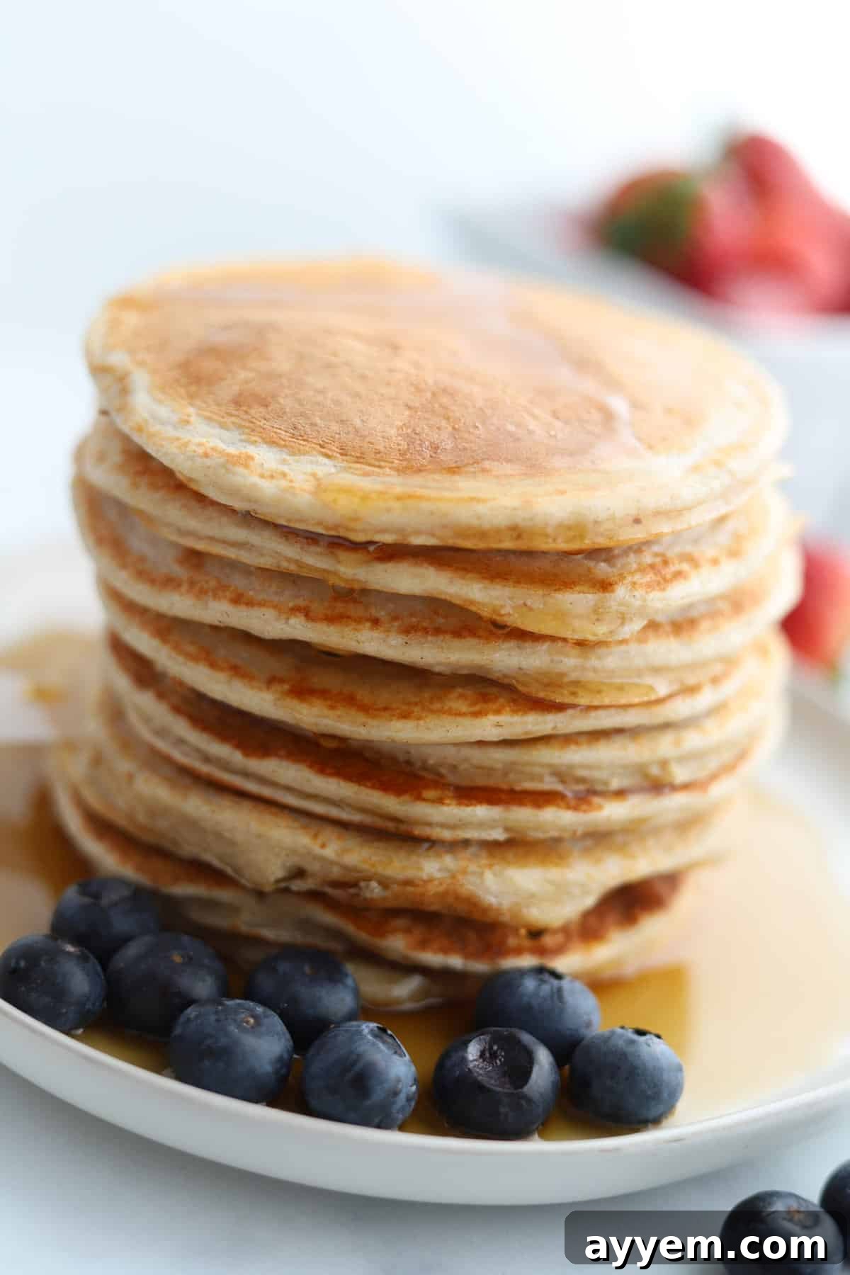 A vibrant, close-up shot of a stack of golden cottage cheese protein pancakes, richly topped with golden syrup and an abundance of fresh blueberries, set on a white plate. This image captures the deliciousness and health appeal of the dish, ready to be enjoyed.