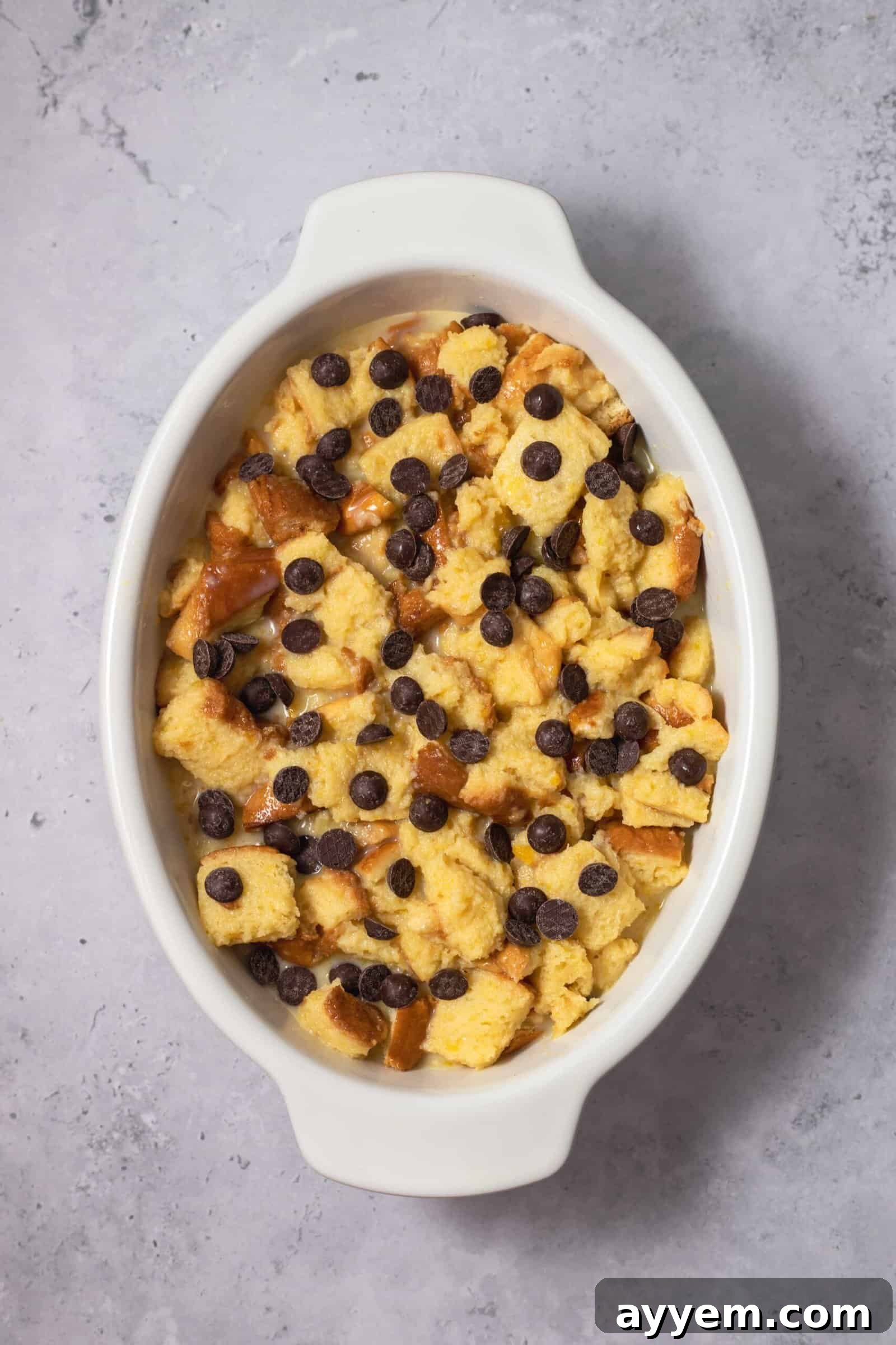 unbaked bread pudding in an oval dish topped with chocolate chips