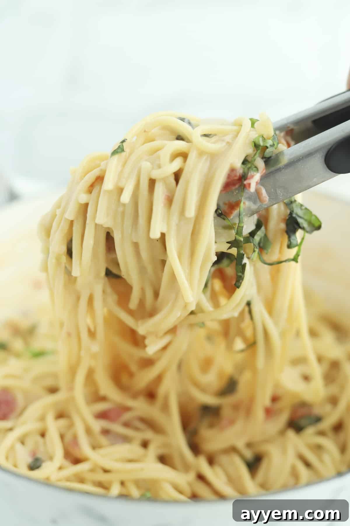 Tongs gently lift a portion of creamy Parmesan pasta from a deep pot, ready to be served.