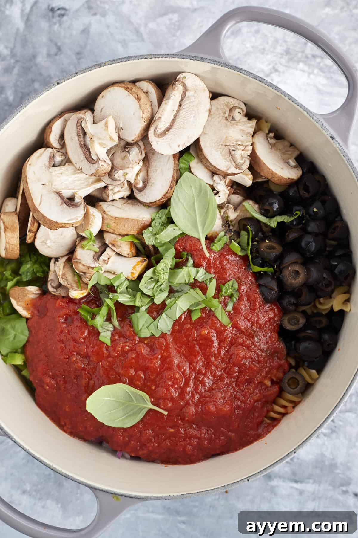 Pizza Night Pasta Pot 4 overhead image of a pot full of uncooked pasta, marinara sauce, fresh herbs, mushrooms, and black olives