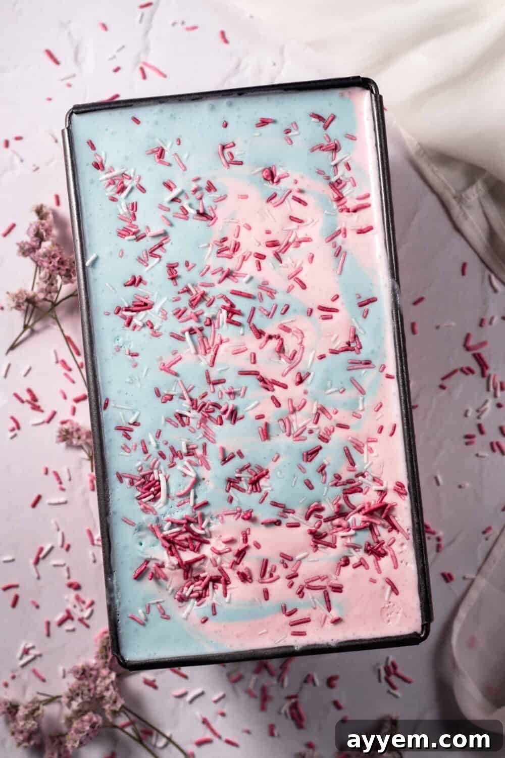 Sweet Dreams Cotton Candy Ice Cream 3 An overhead view of a tub of homemade cotton candy ice cream, generously topped with pink and white sprinkles, highlighting its creamy texture and inviting colors.