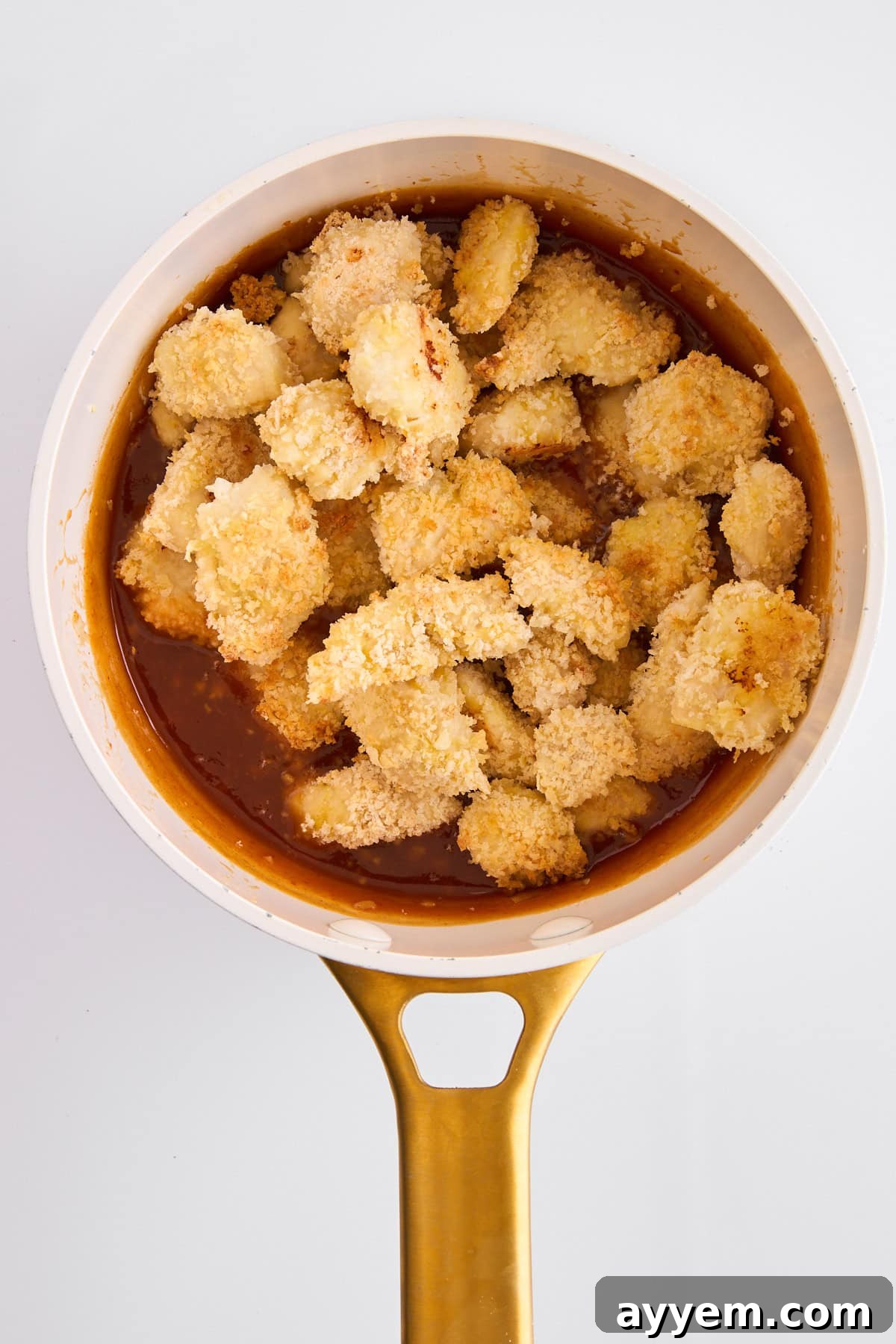 Breaded cooked chicken pieces being tossed in orange sauce in a pot.