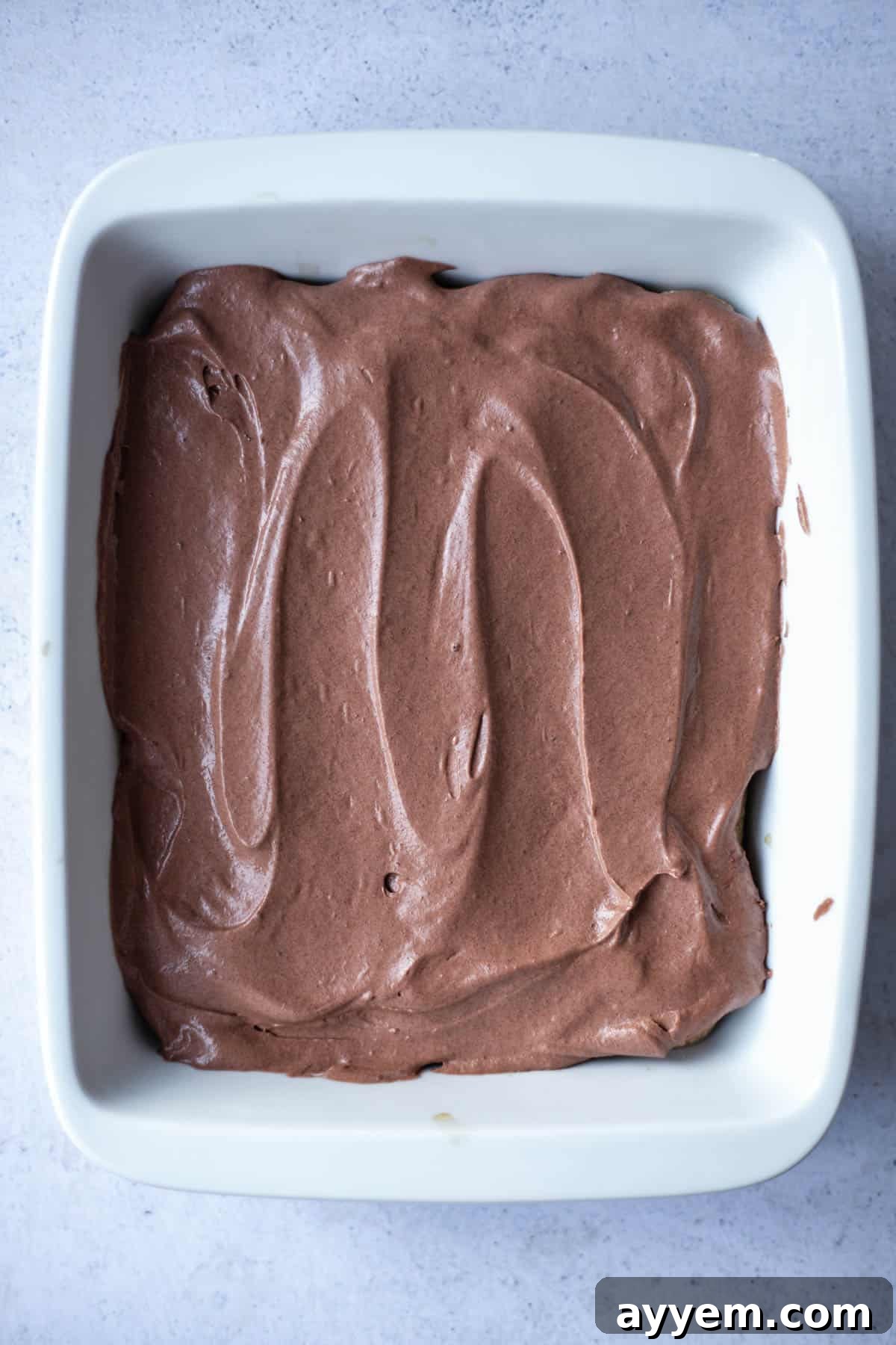 A close-up view of the smooth, even layer of chocolate mascarpone filling, covering the ladyfingers in a baking dish.