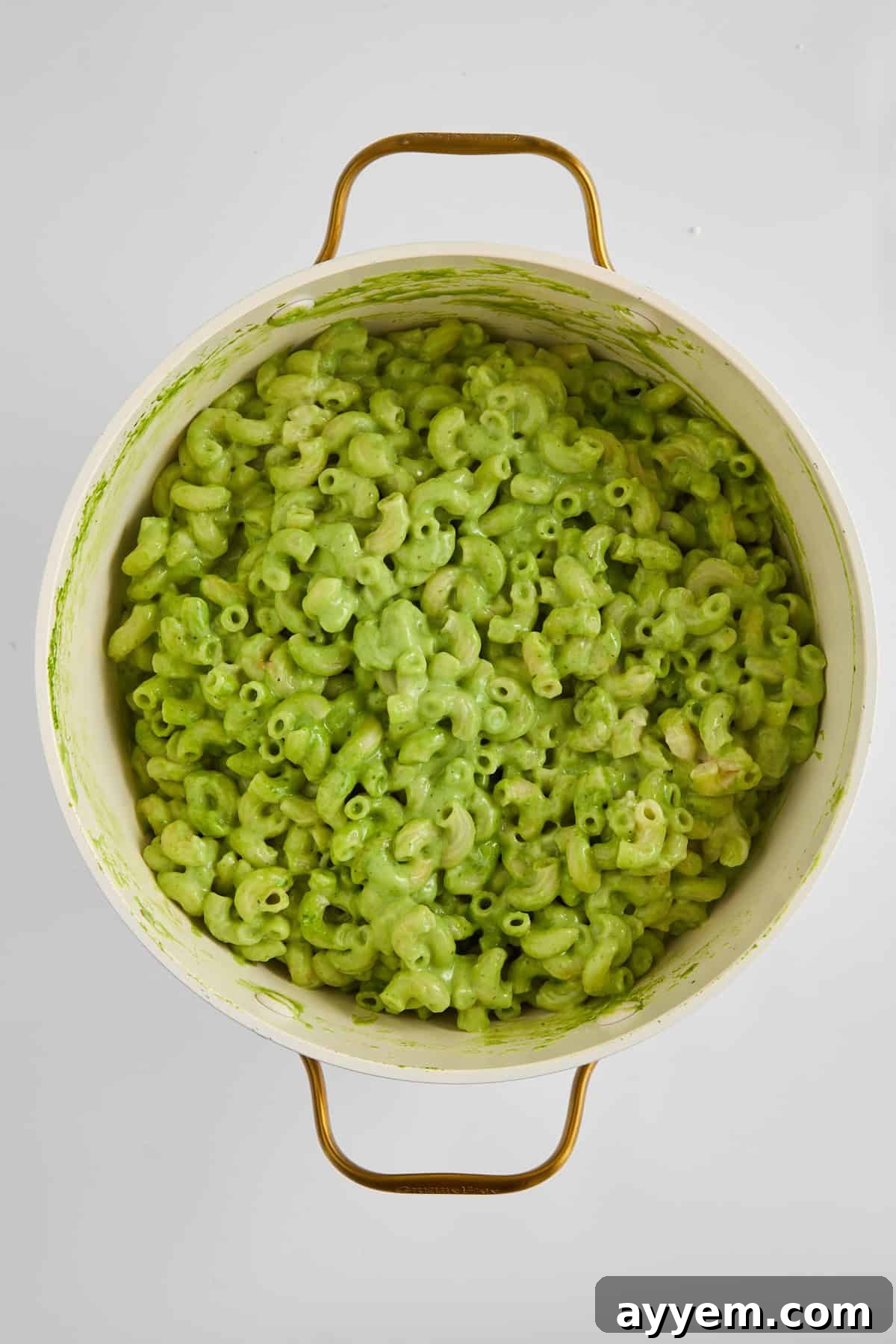Cooked pasta being stirred into the creamy green cheese sauce.