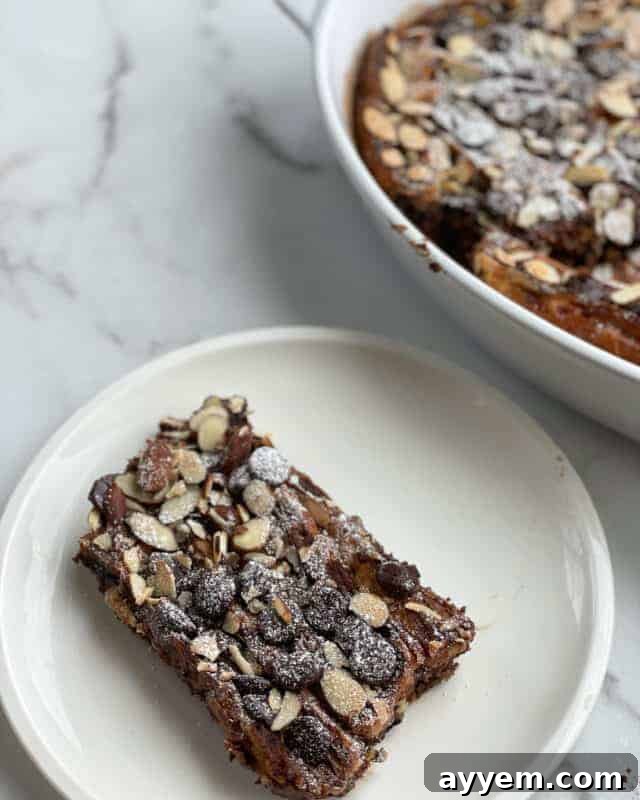 A perfectly golden slice of Chocolate French Toast, generously drizzled with melted dark chocolate and sprinkled with crunchy almond slices, resting on a white plate ready to be enjoyed.