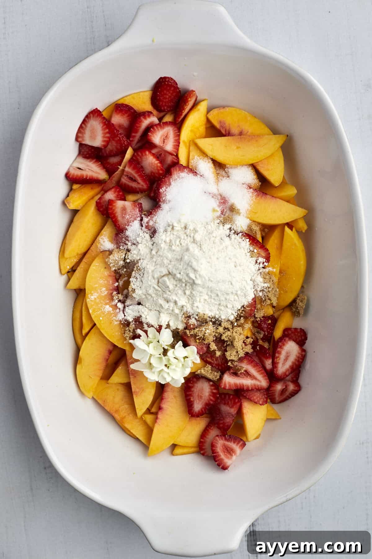 Sliced peaches and strawberries in a baking dish, coated with granulated sugar, brown sugar, cinnamon, and flour, ready for baking.