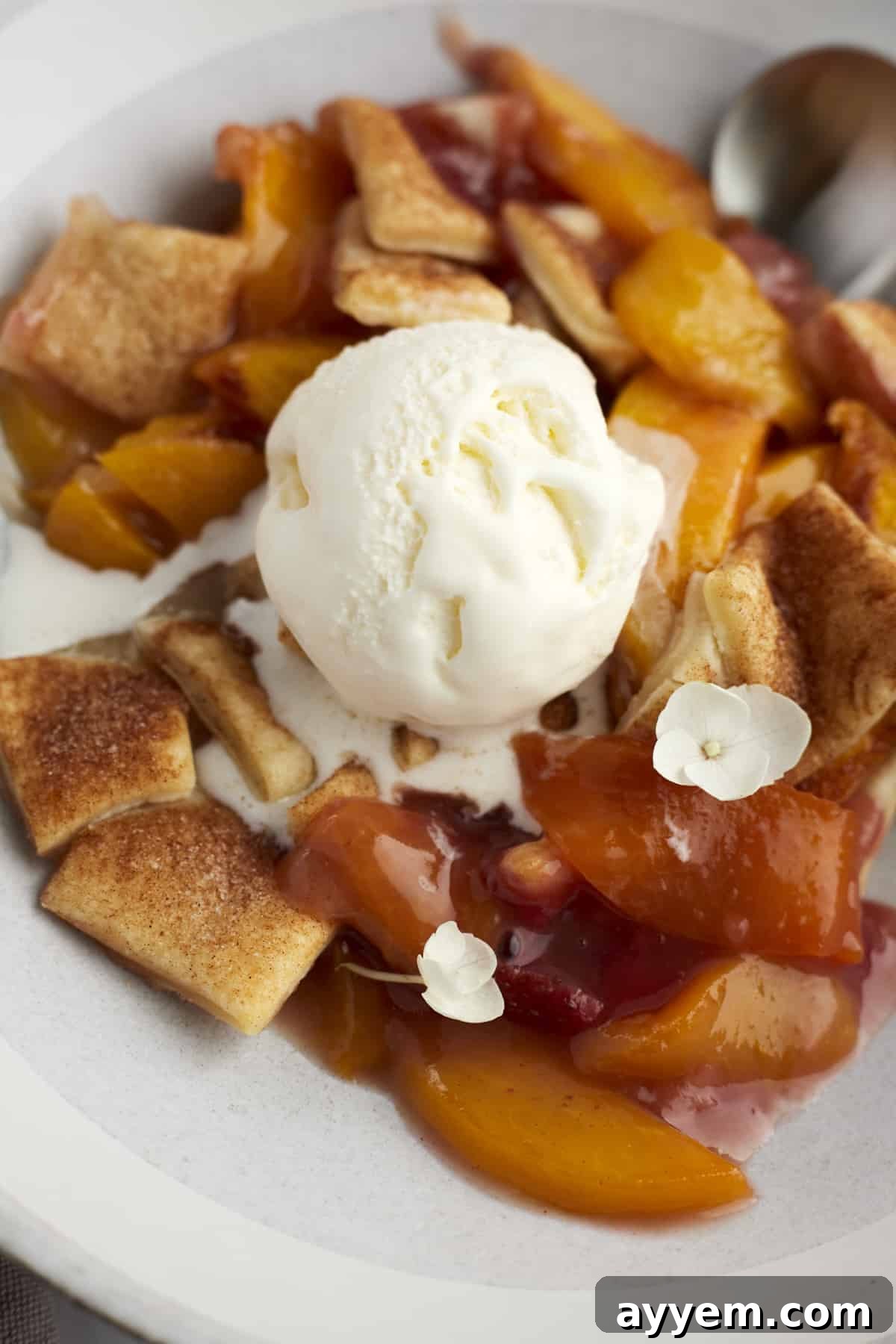 Close-up image of a serving of peach strawberry cobbler, generously topped with a melting scoop of vanilla ice cream, highlighting the rich fruit filling and golden crust.