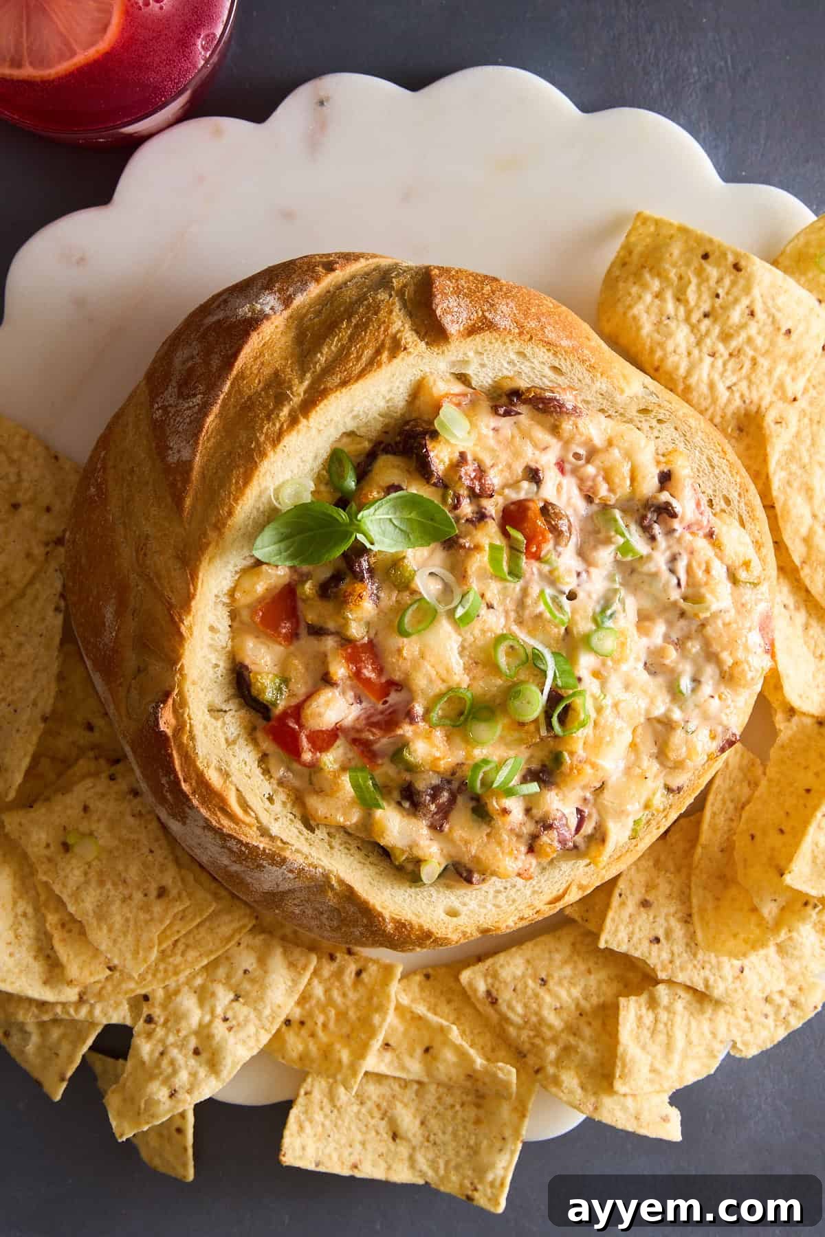 A sourdough bread bowl brimming with a golden cheese dip, surrounded by a generous scattering of crunchy tortilla chips, ready to be enjoyed.