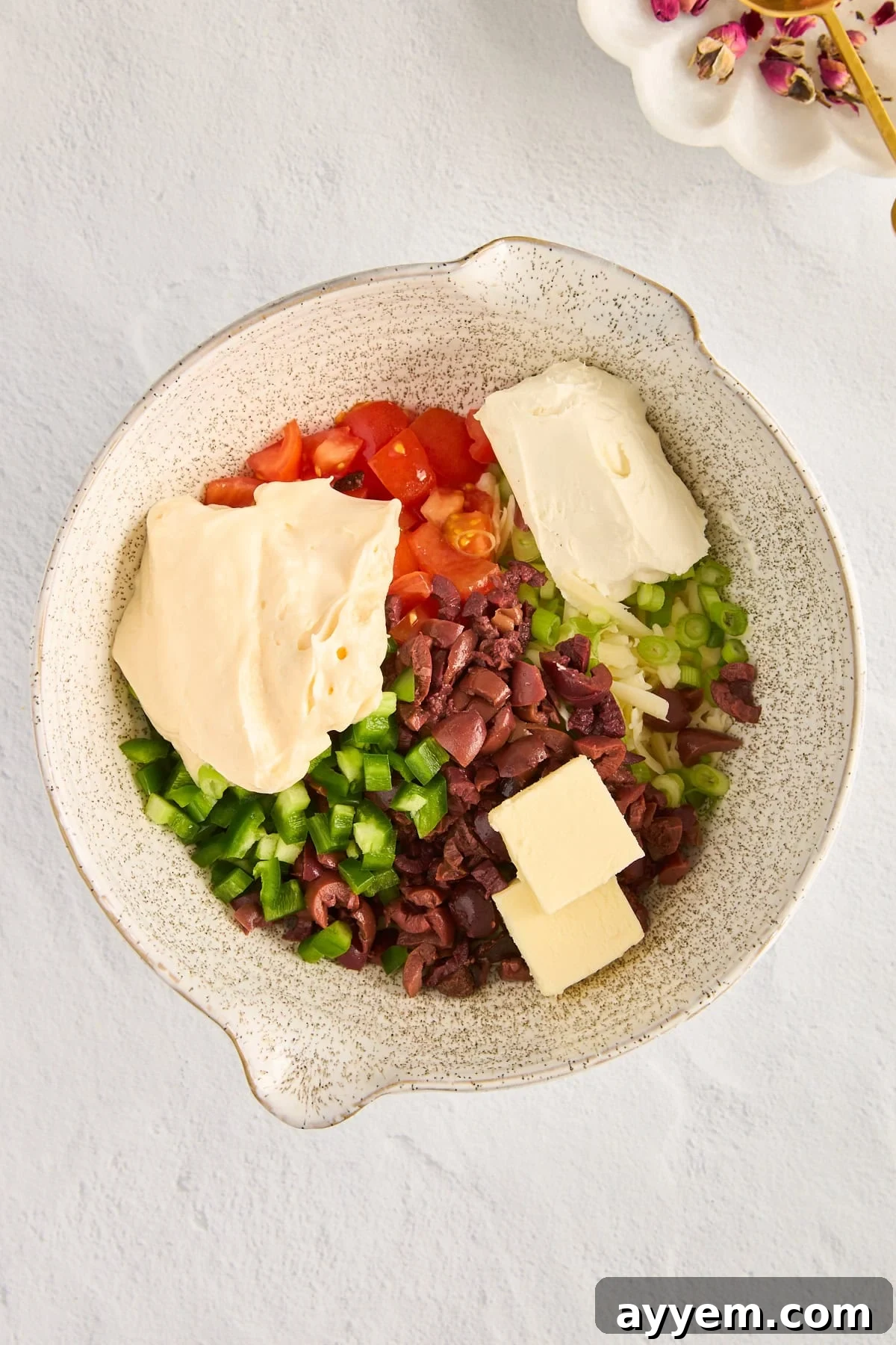 A vibrant mix of bell peppers, tomatoes, black olives, and shredded cheese in a large mixing bowl, showcasing the fresh ingredients for the dip.