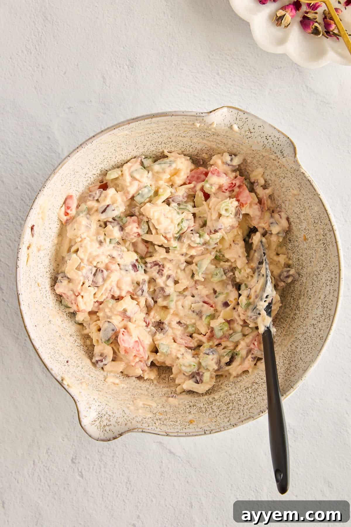 A close-up view of the creamy cheese dip mixture in a bowl before baking, with visible bits of green onion, tomatoes, and black olives.