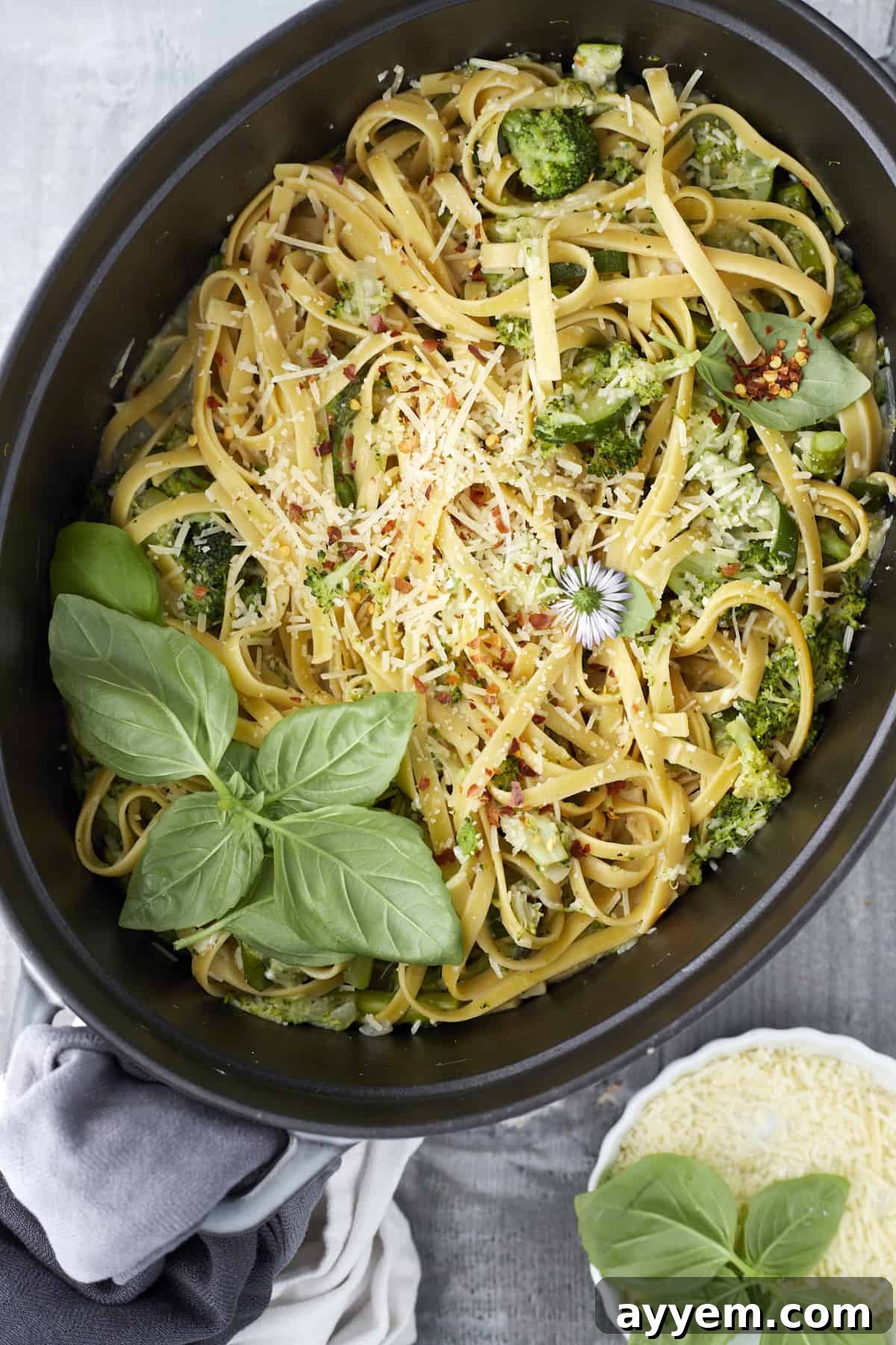 Overhead image of pasta with veggies in a large pot topped with cheese, herbs, and seasonings, ready to be served.