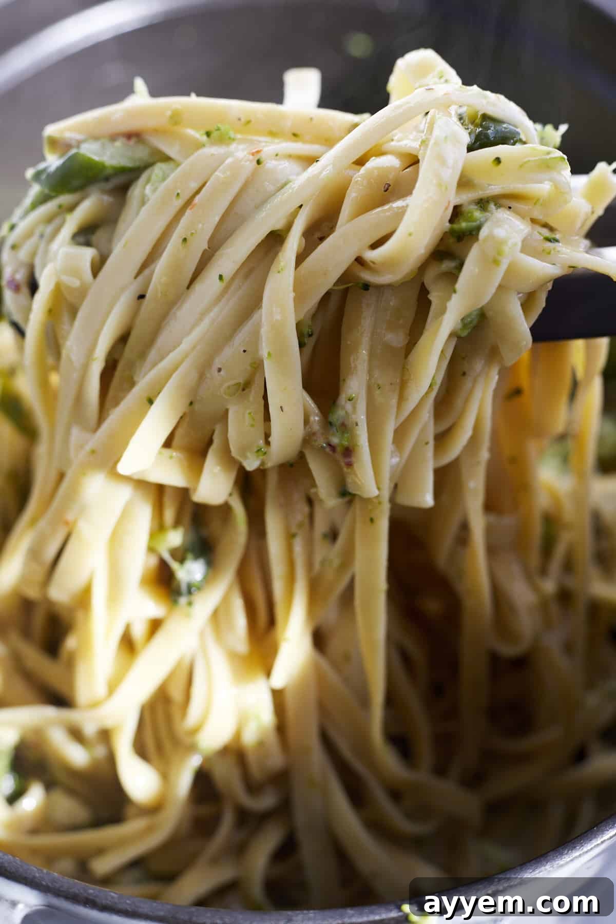 A serving of pasta with veggies being lifted with tongs, showcasing the creamy sauce and mixed vegetables.