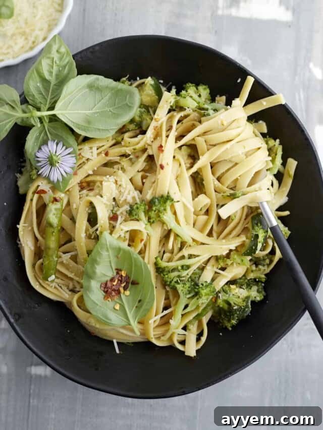 Overhead image of a black bowl of pasta with veggies, beautifully presented with fresh herbs.