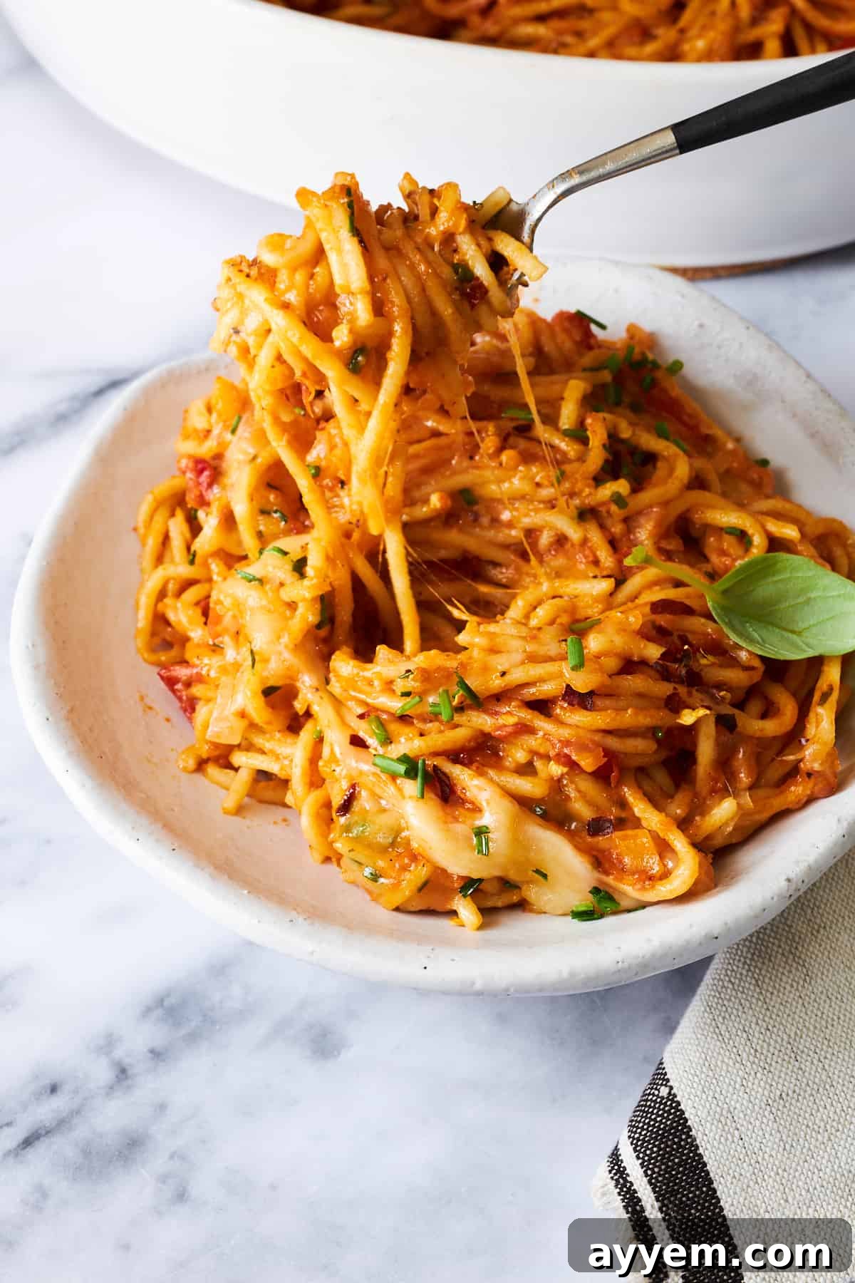 A fork lifting a perfect bite of oven-baked spaghetti from a plate, showcasing the melted cheese and rich sauce clinging to the pasta strands.