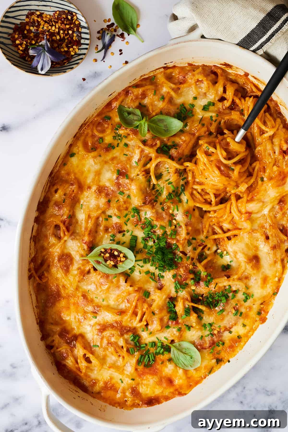A large oval baking dish full of oven-baked spaghetti, golden and bubbly with melted cheese, ready to be served.