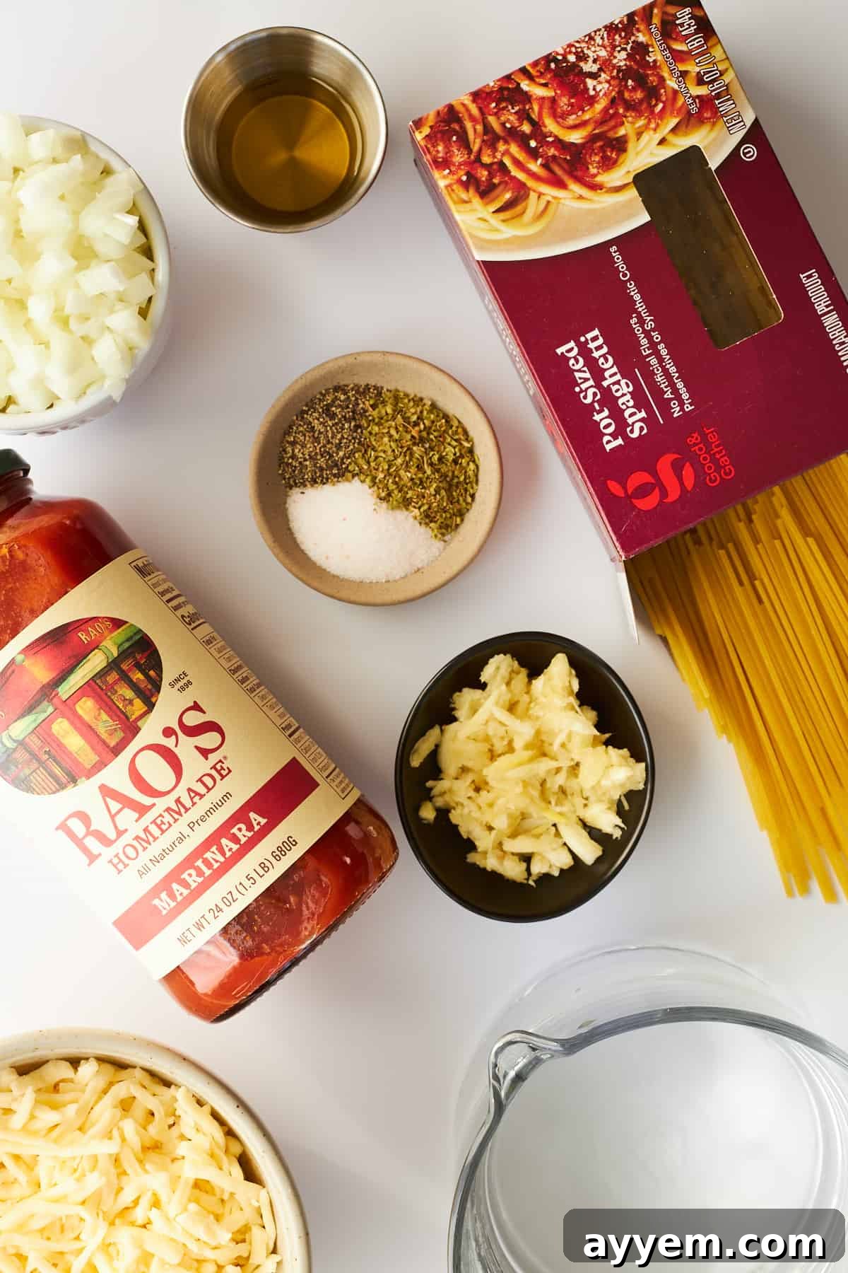 A selection of fresh ingredients laid out, including uncooked spaghetti, a jar of rich pasta sauce, fragrant herbs, and a bulb of garlic, prepared for making a delicious oven-baked spaghetti.