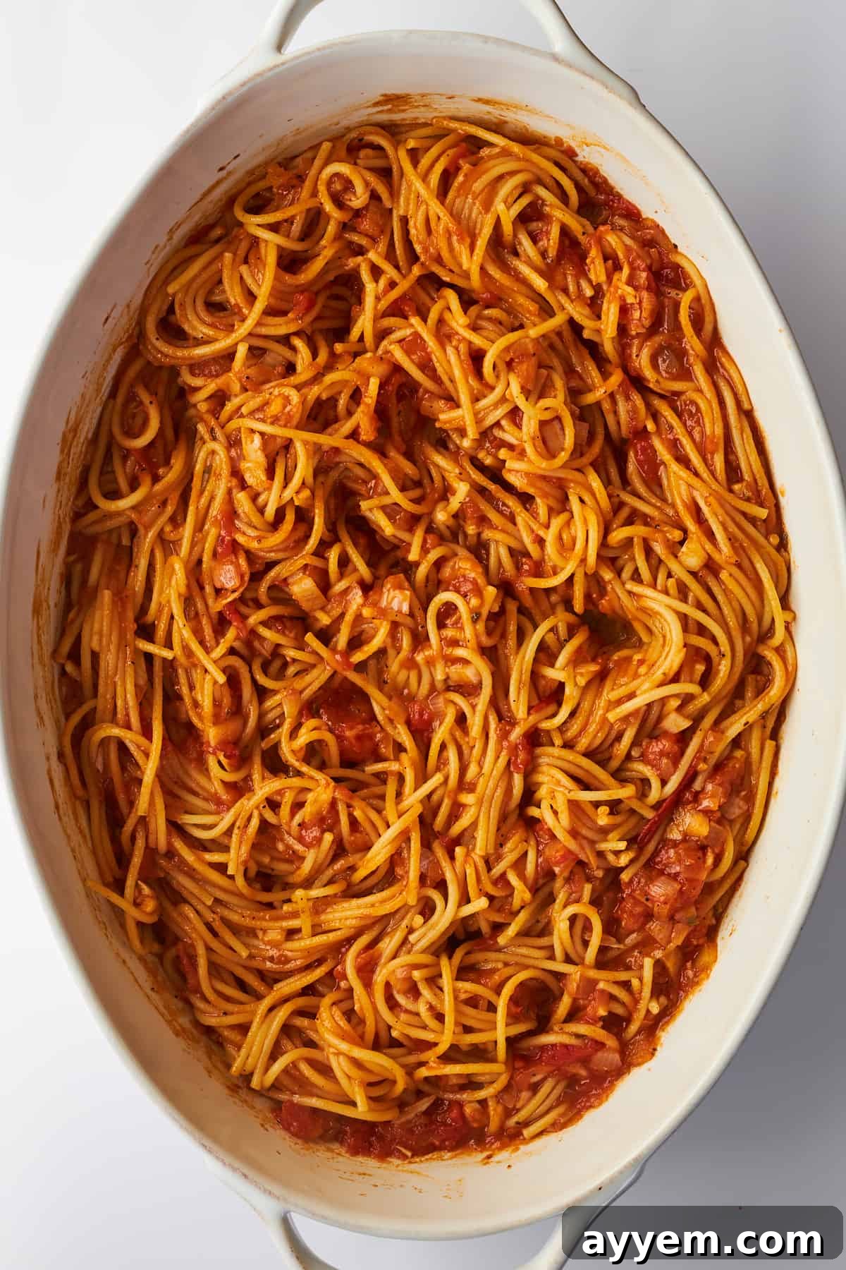 A large oval baking dish full of perfectly baked spaghetti, with the pasta cooked al dente and coated in a rich tomato sauce, ready for its cheesy topping.