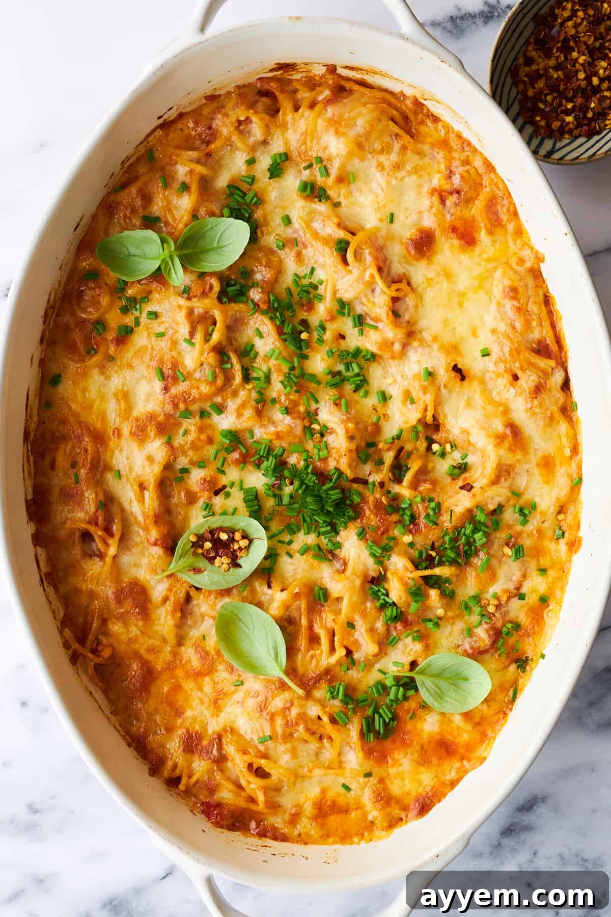 A close-up shot of cheesy baked spaghetti in an oval baking dish, with the golden-brown melted cheese glistening and inviting diners to dig in.