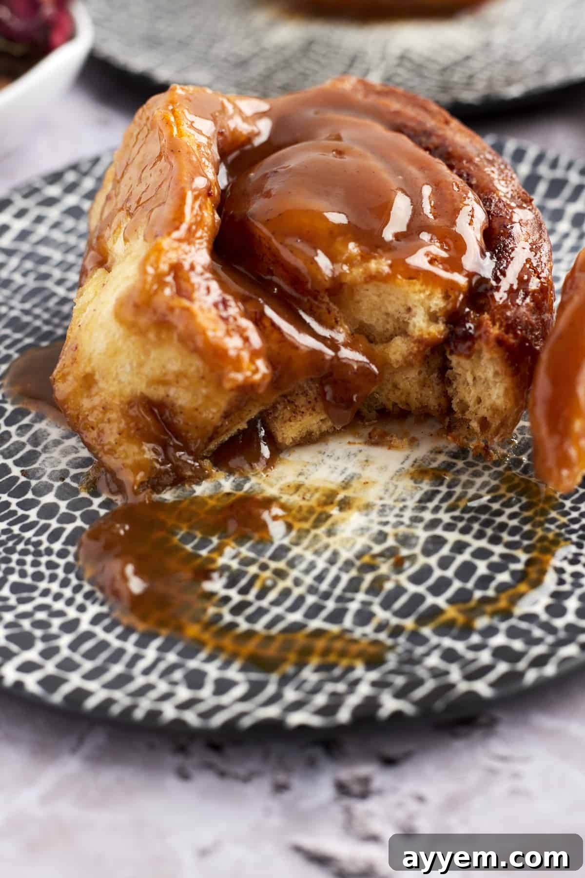 A delectable caramel macchiato cinnamon roll on a plate, with a bite taken out, showcasing its soft, layered texture and rich glaze.