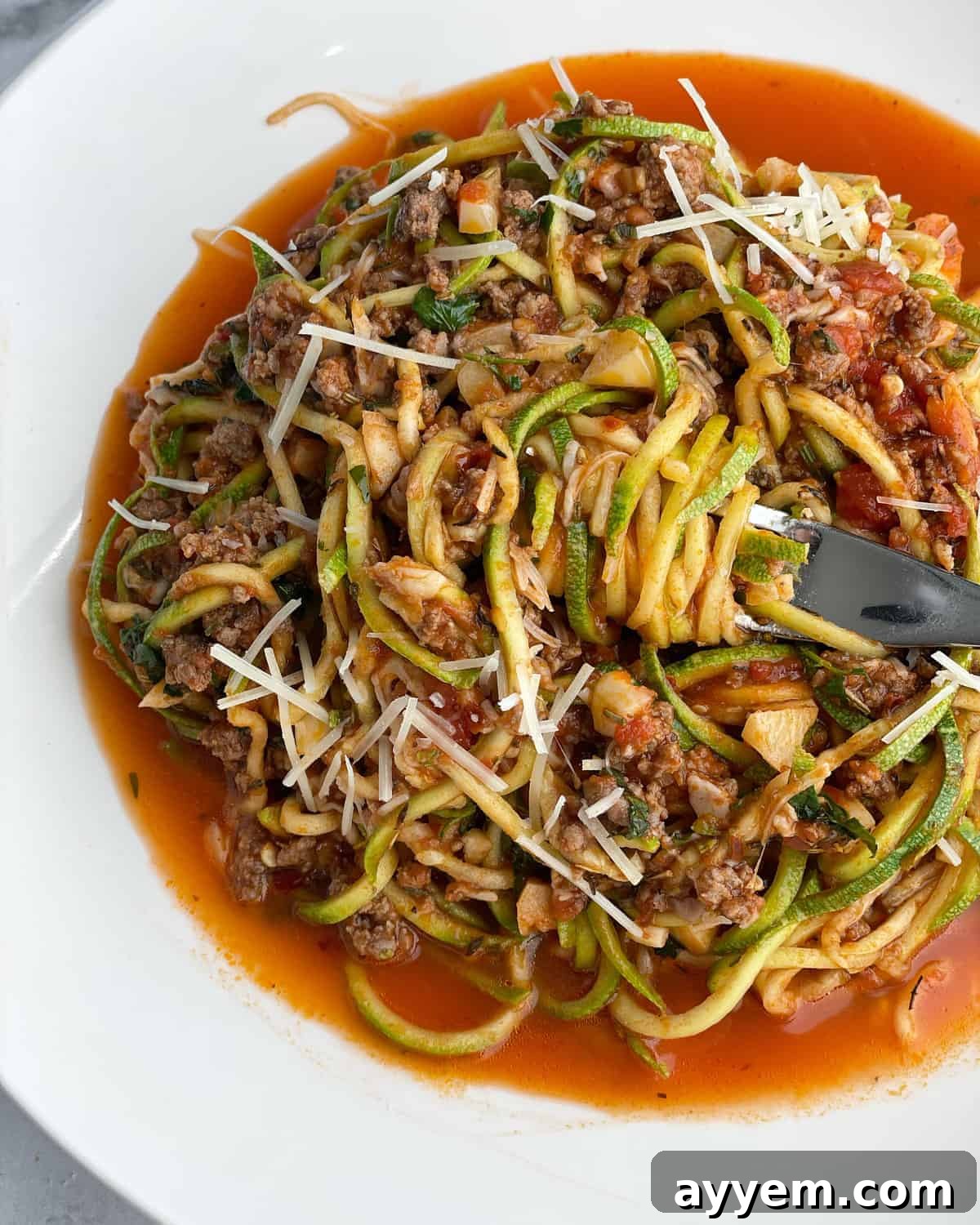A bowl of low carb baked spaghetti zoodles with a bite being twirled around a fork, showcasing the healthy meal.