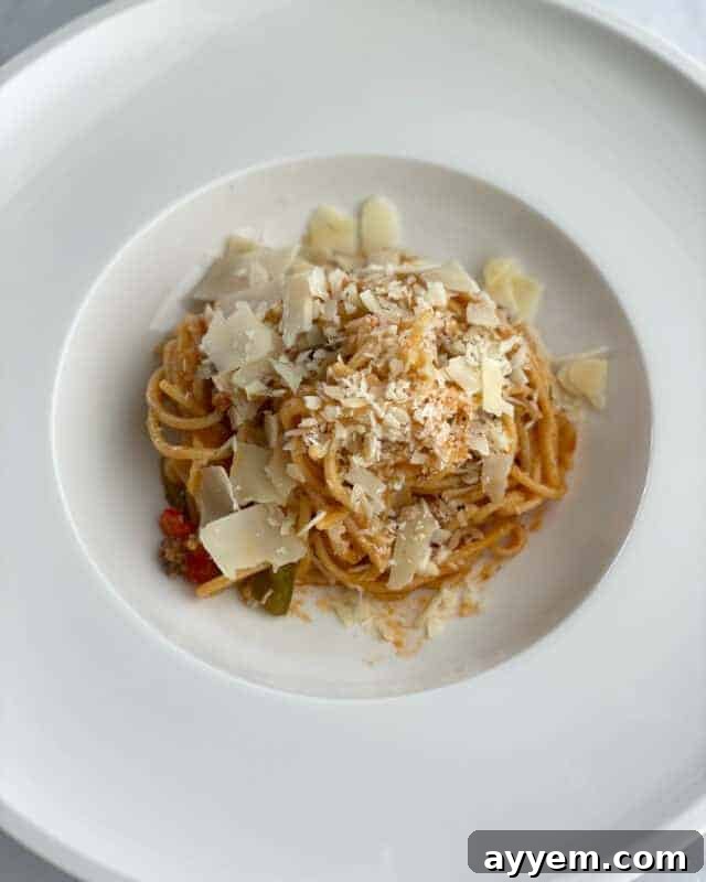 A plate with a serving of baked spaghetti bolognese recipe topped with shaved parmesan.