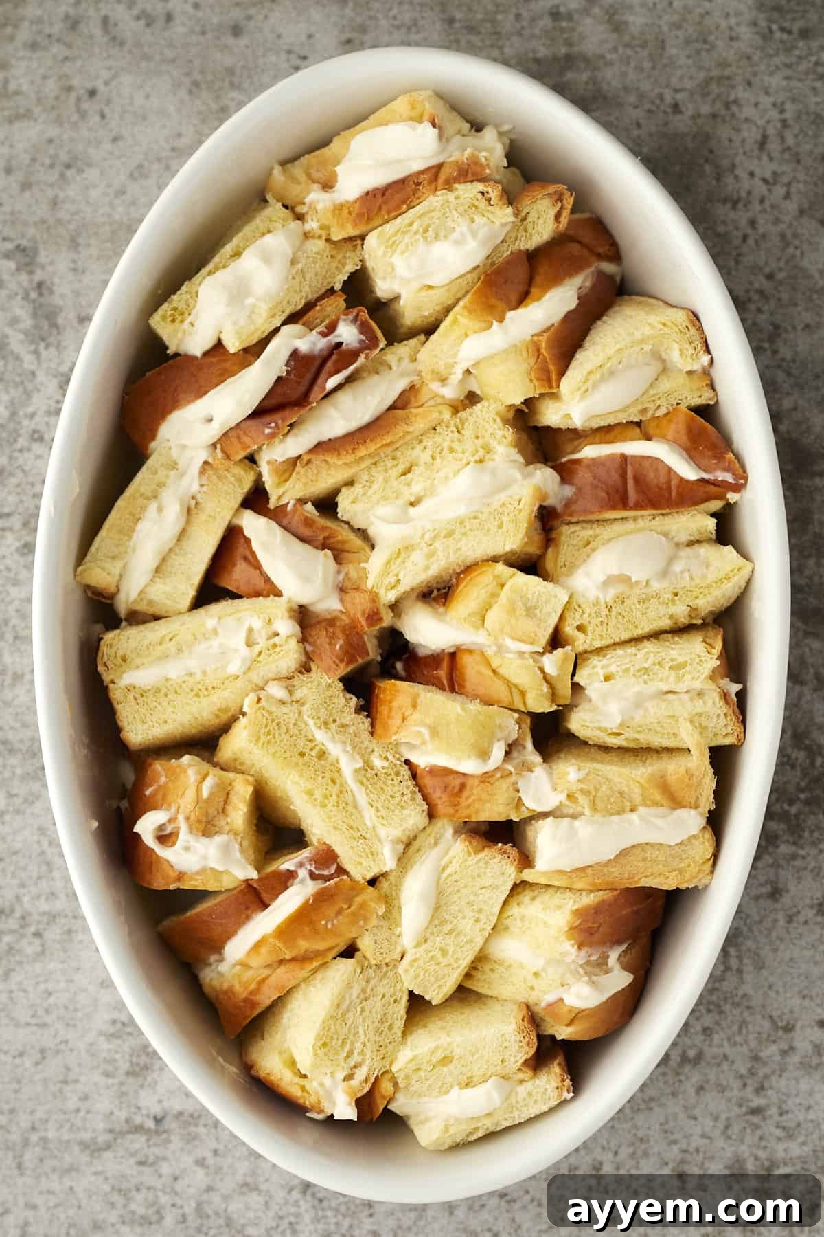Ricotta Cream French Toast Bake 3 Close-up of cannoli stuffed french toast pieces arranged in an oval baking dish before baking.