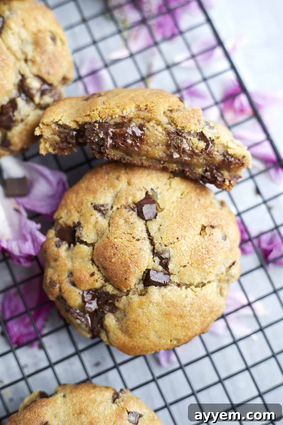 A large ultimate chocolate chip cookie is meticulously sliced in half, offering a peek into its molten, gooey chocolate-laden interior, resting on a wire cooling rack.