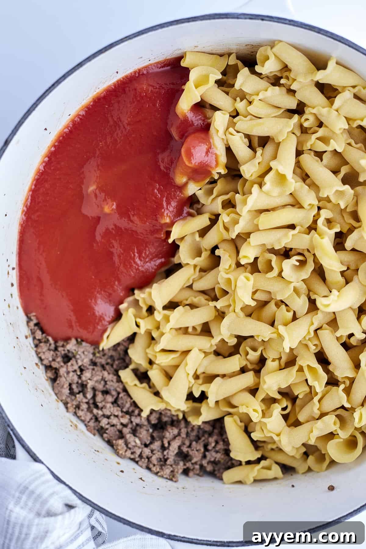 cooked ground beef with sauce and uncooked pasta in a pot.