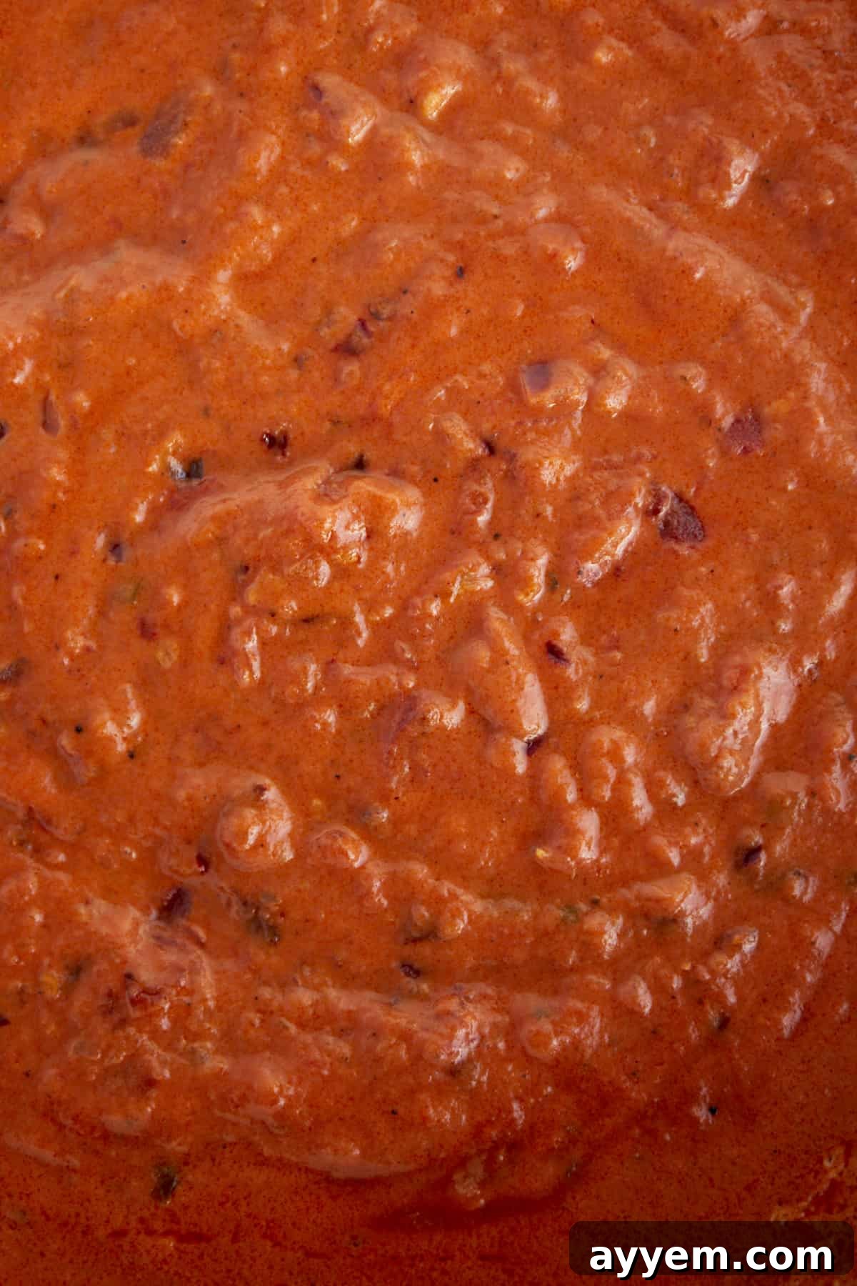A close-up view of a rich, red spicy pasta sauce simmering, showcasing its creamy texture and hints of chili flakes.