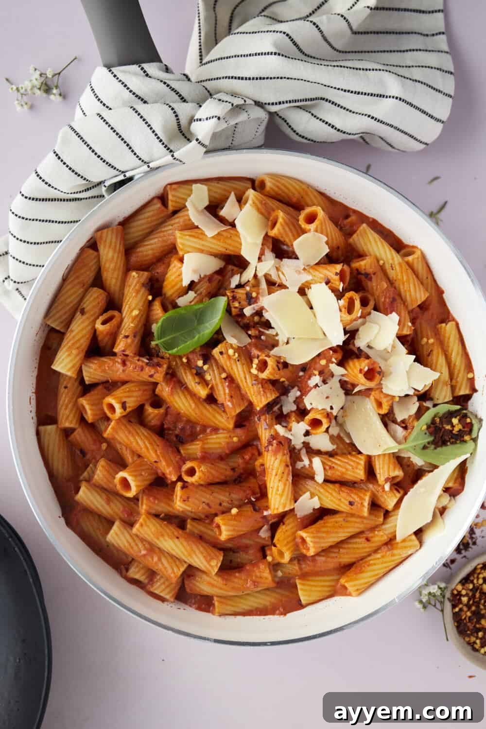 A large, inviting bowl filled with spicy rigatoni pasta, generously topped with freshly shaved Parmesan cheese, glistening with rich sauce.