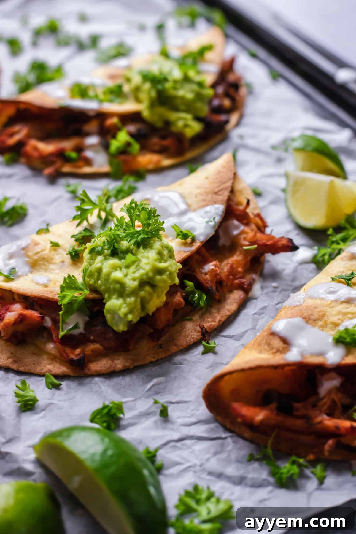 close up image of baked shredded chicken tacos topped with guacamole and fresh herbs