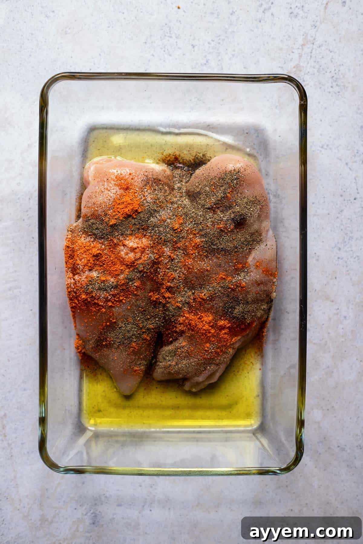 two raw chicken breasts in a baking dish topped with oil and spices