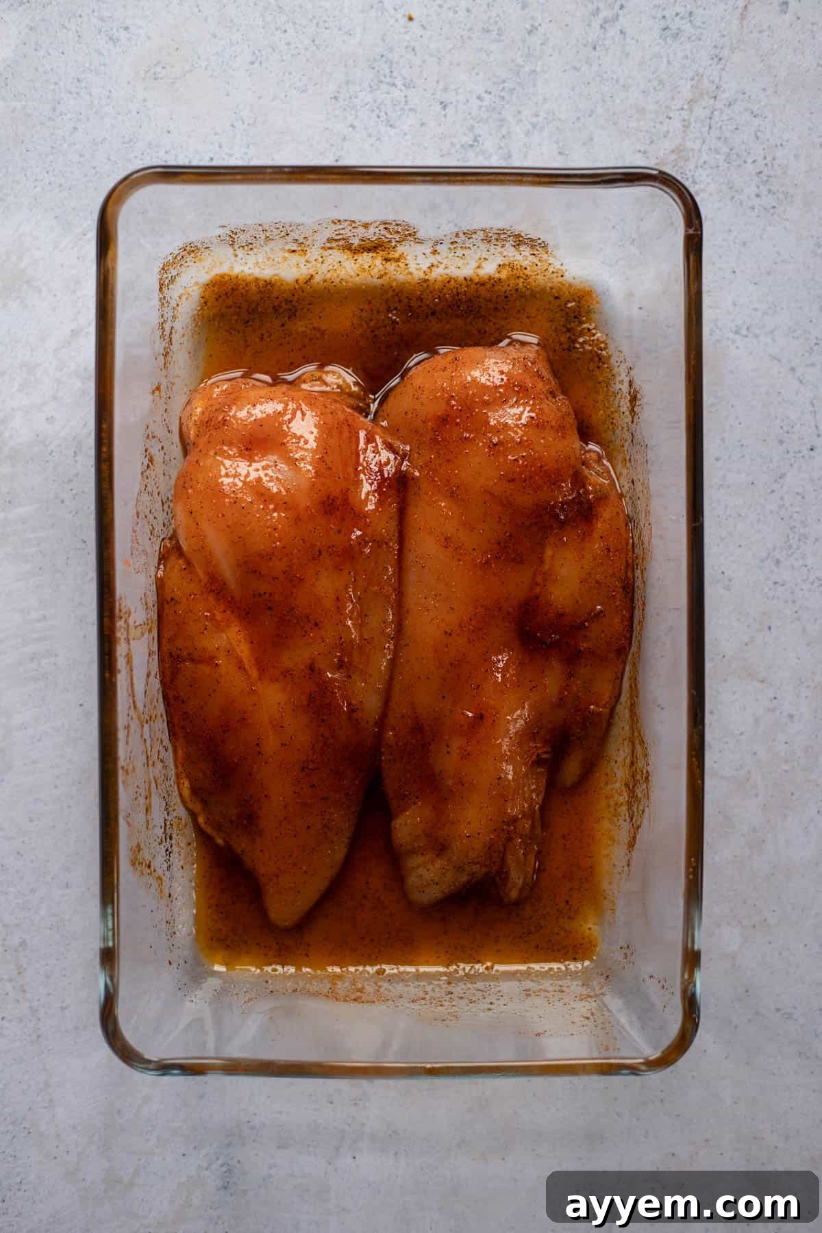two raw chicken breasts in a baking dish rubbed with seasonings