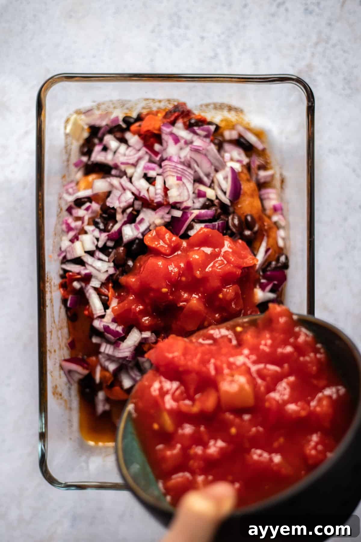 raw seasoned chicken topped with black beans and diced red onions with salsa being poured on top